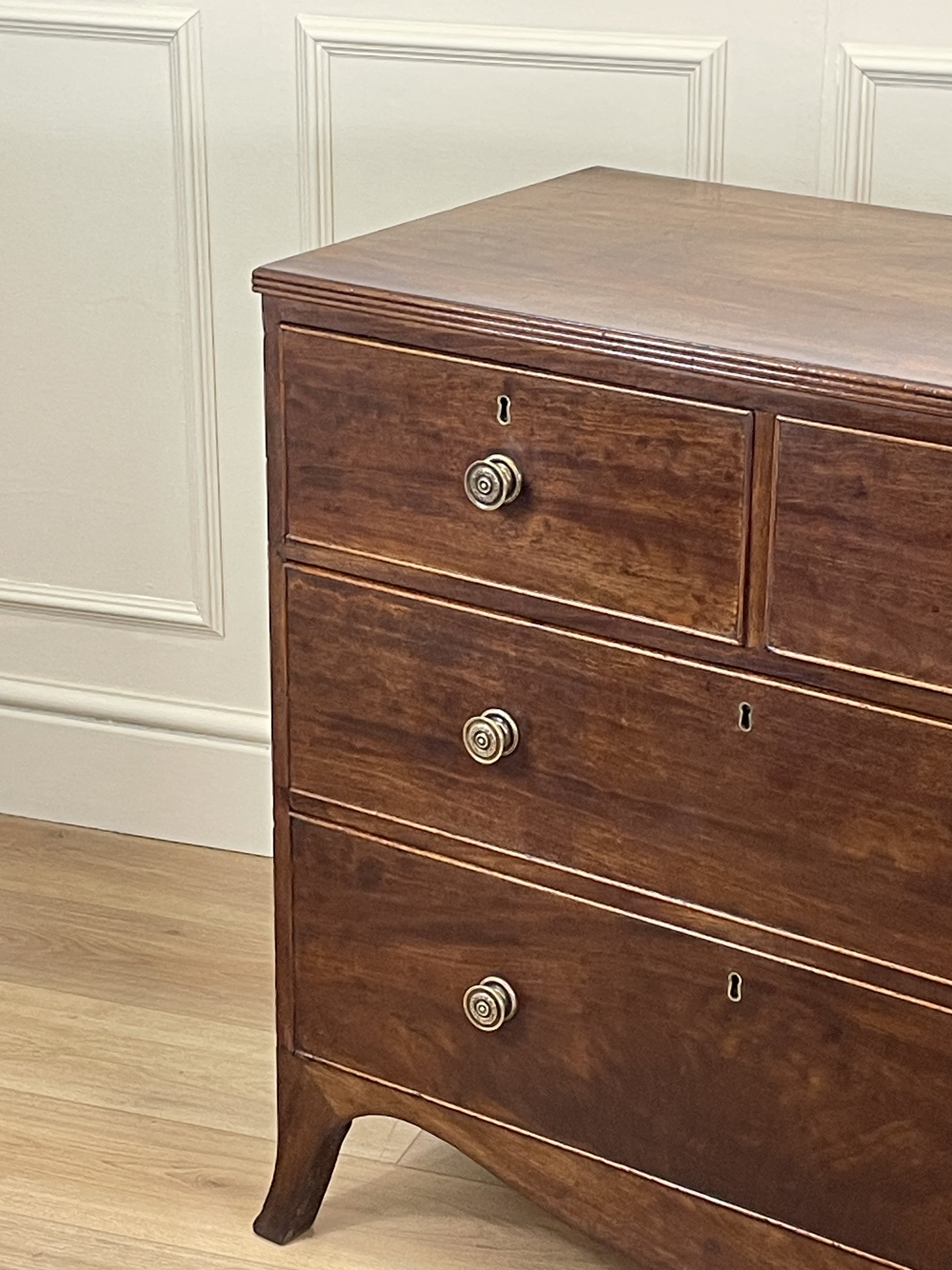 Wooden dresser with three drawers against a white paneled wall.