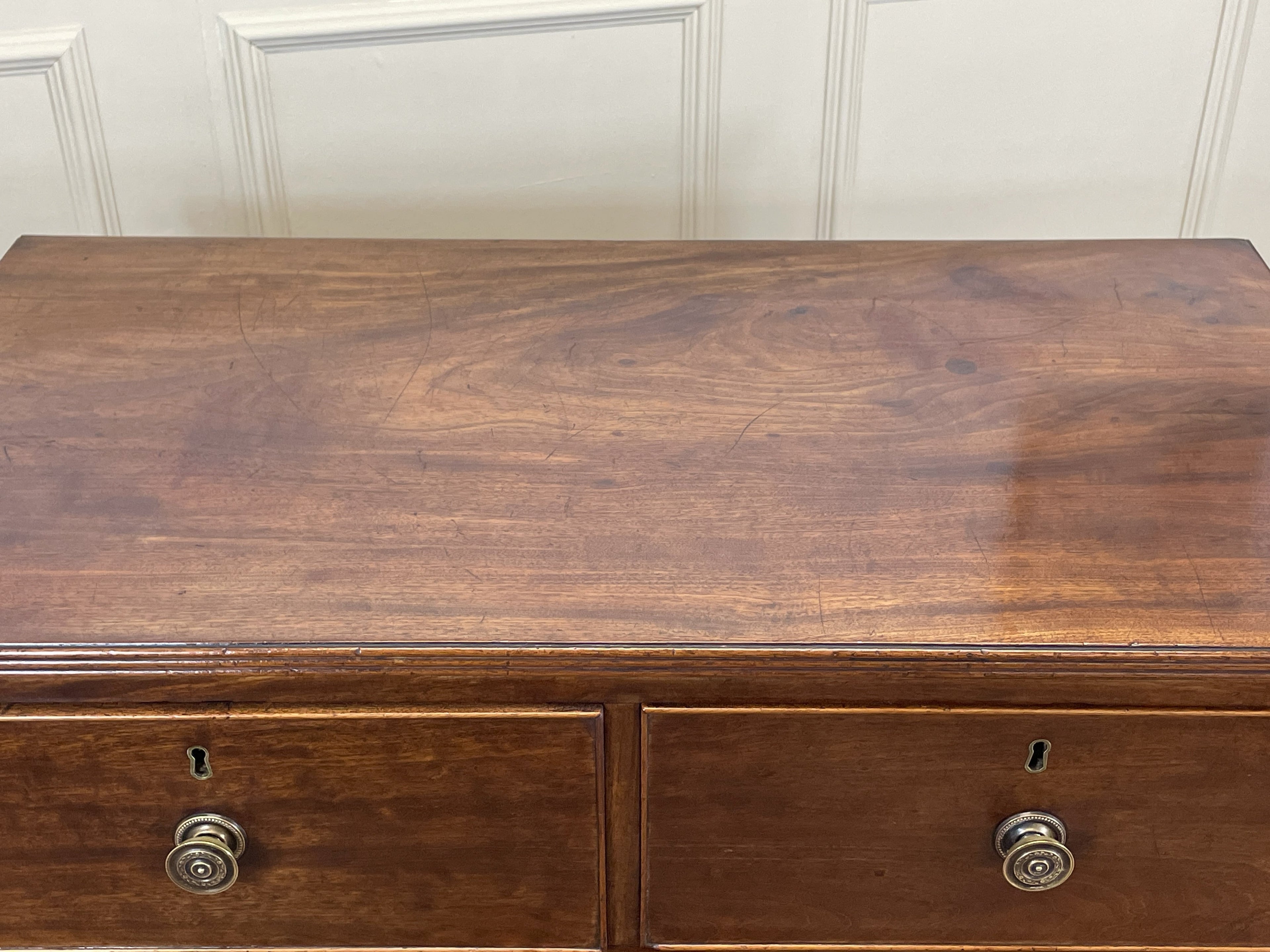 Wooden dresser with two drawers against a white paneled wall.