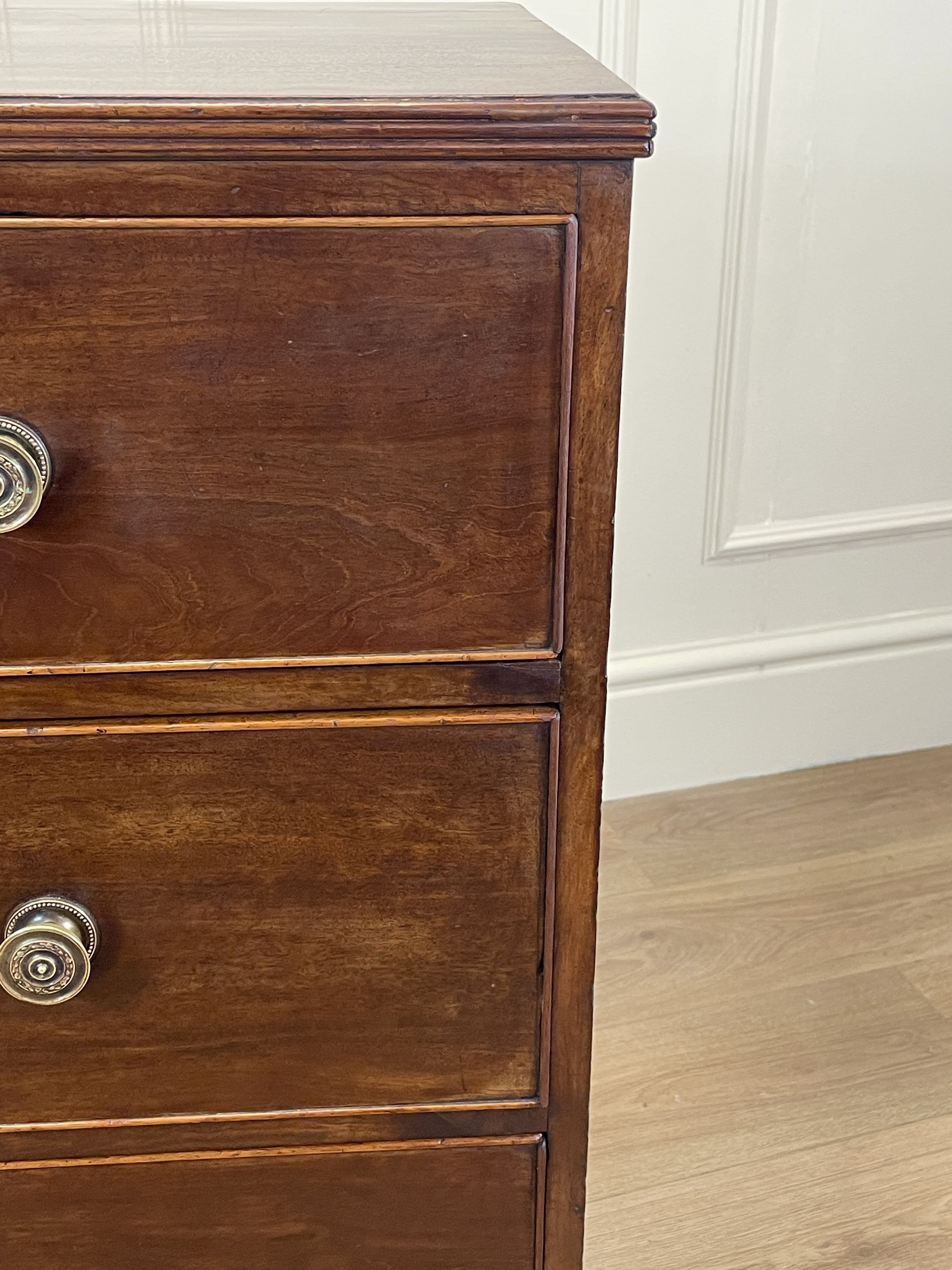 Wooden dresser with two drawers and brass handles against a white paneled wall.