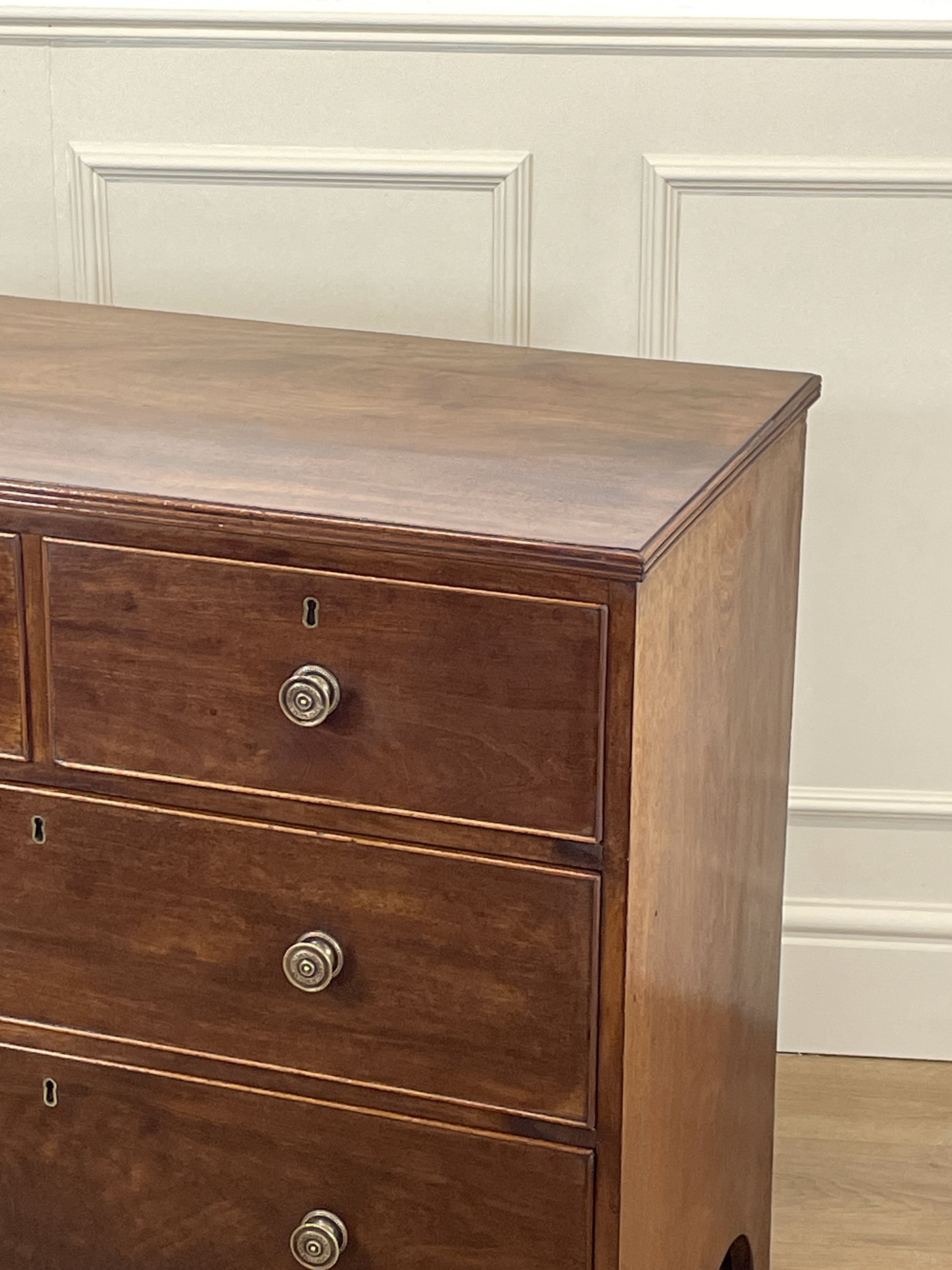 Wooden dresser with three drawers against a white paneled wall.
