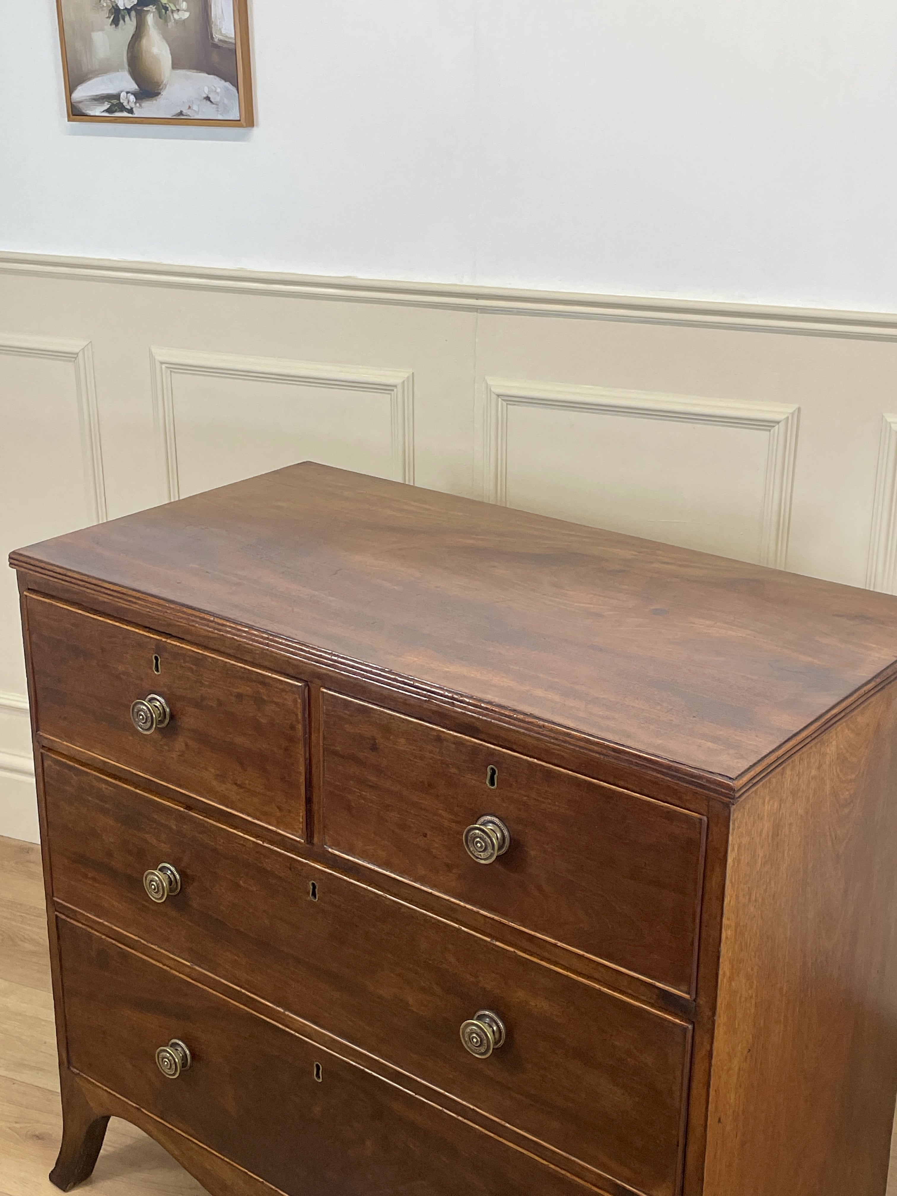 Wooden dresser with three drawers against a white paneled wall.