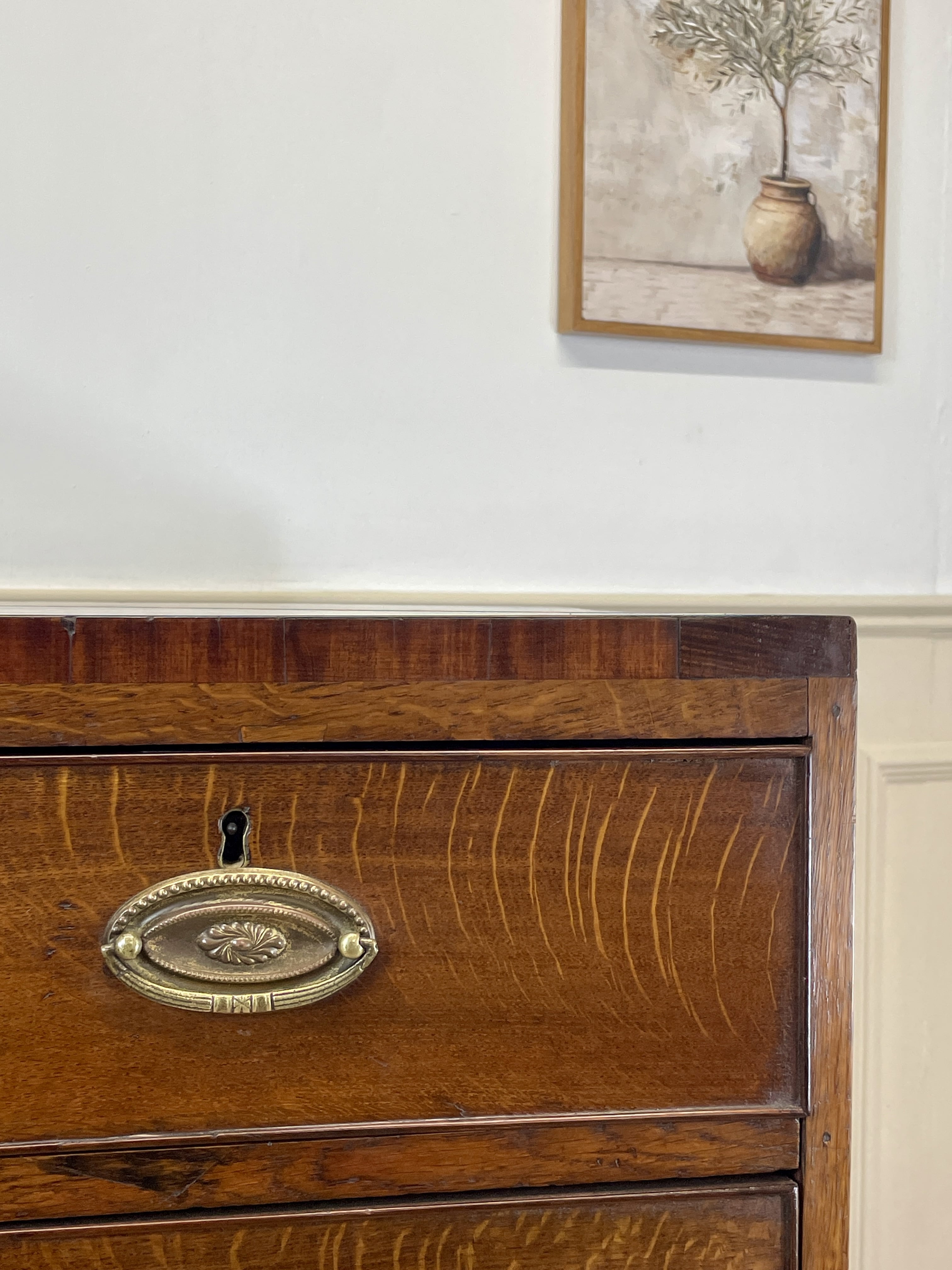 Wooden dresser with brass handle and framed artwork on the wall.