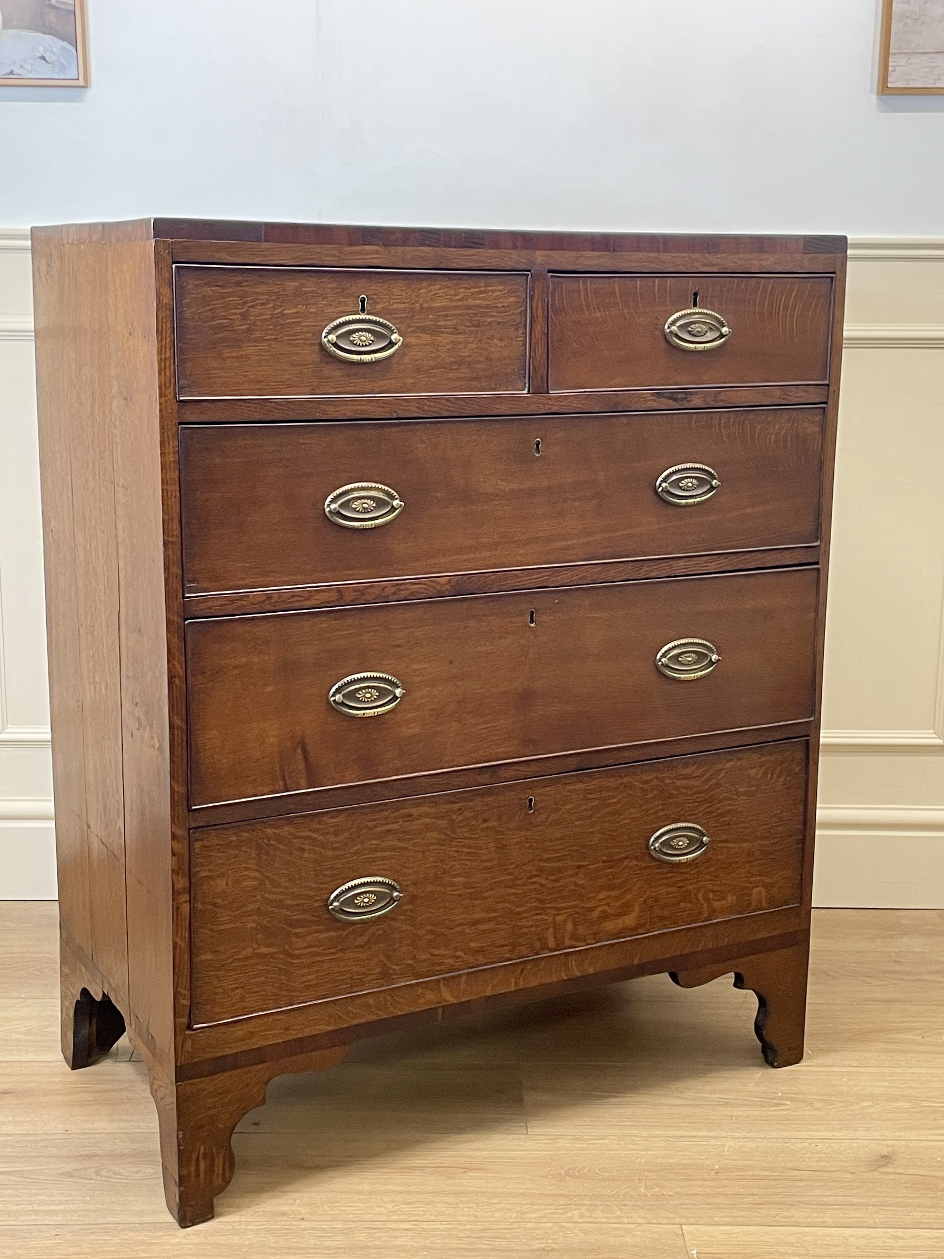 Wooden dresser with four drawers and brass handles on a wooden floor.