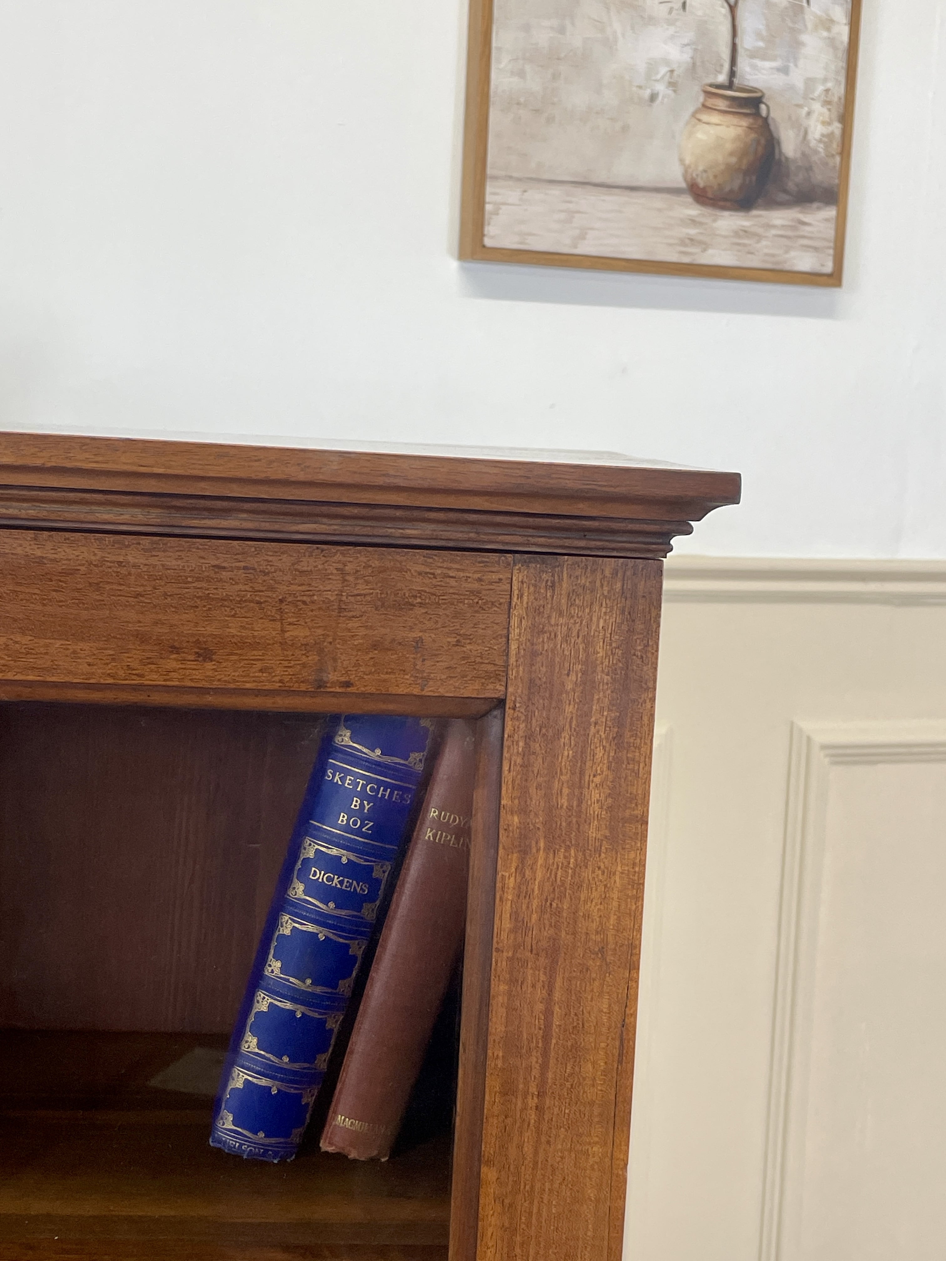 Wooden shelf with a blue book and a brown book, framed picture on the wall.