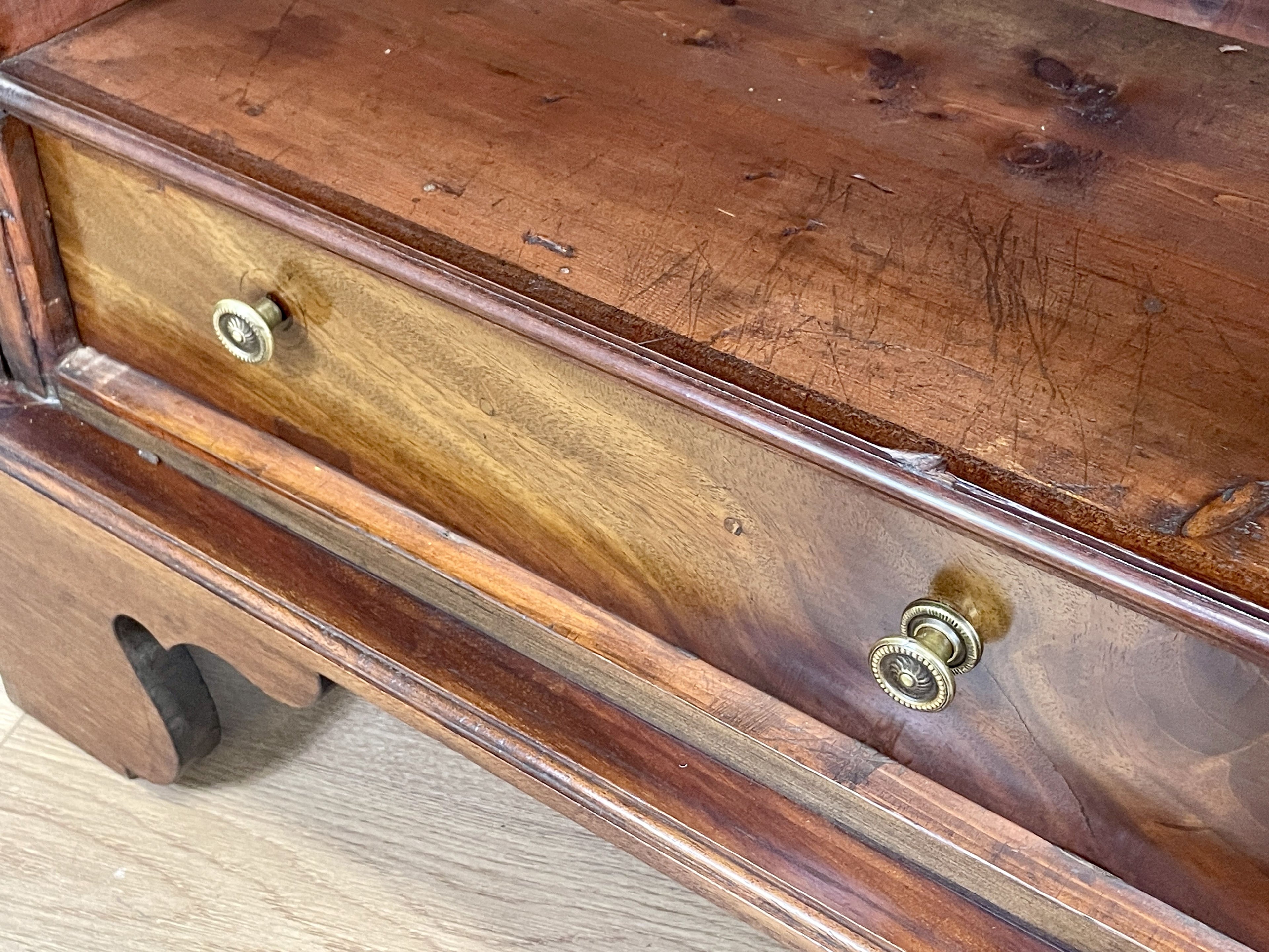 Close-up of a wooden drawer with brass handles on a light wood floor.