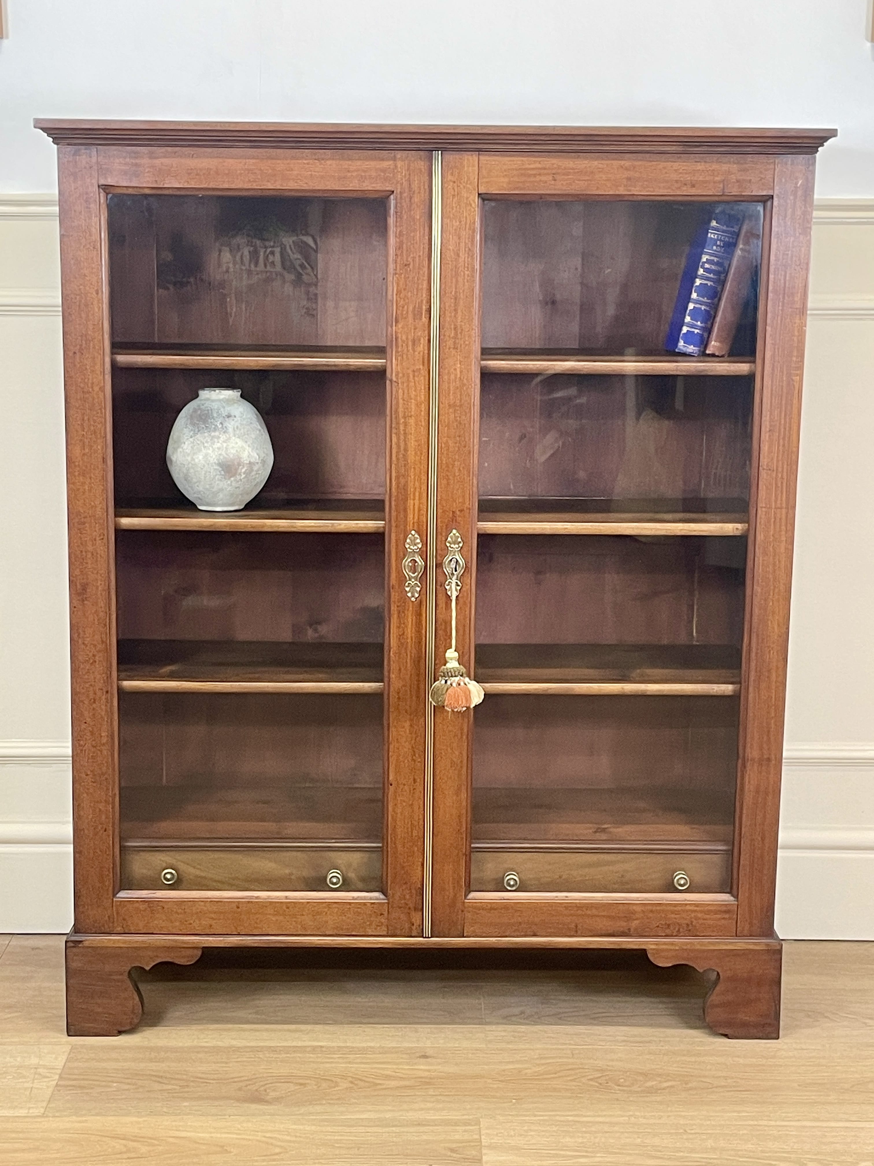 Wooden display cabinet with glass doors against a white wall.