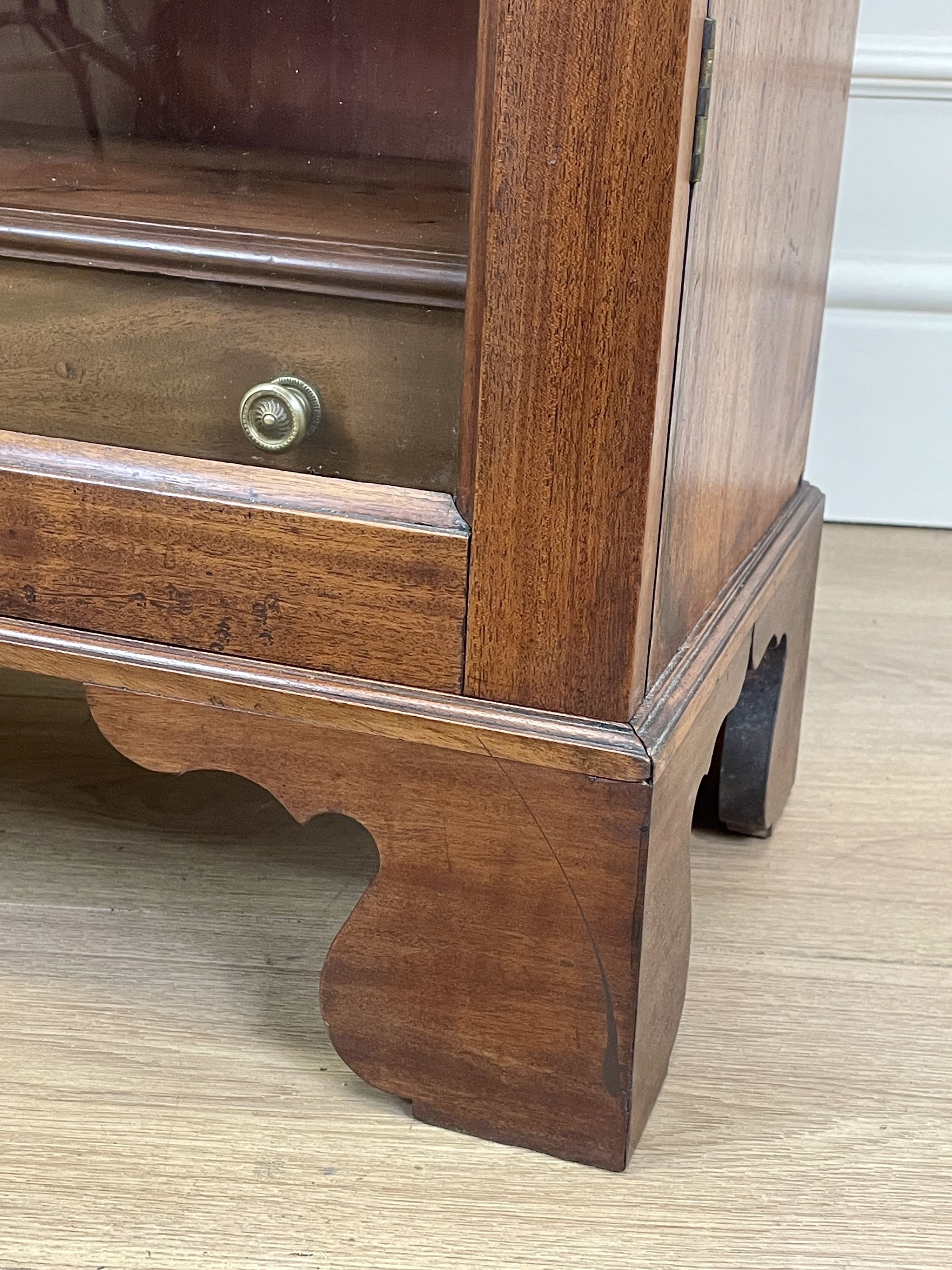 Wooden cabinet with glass door and metal handle on a wooden floor.