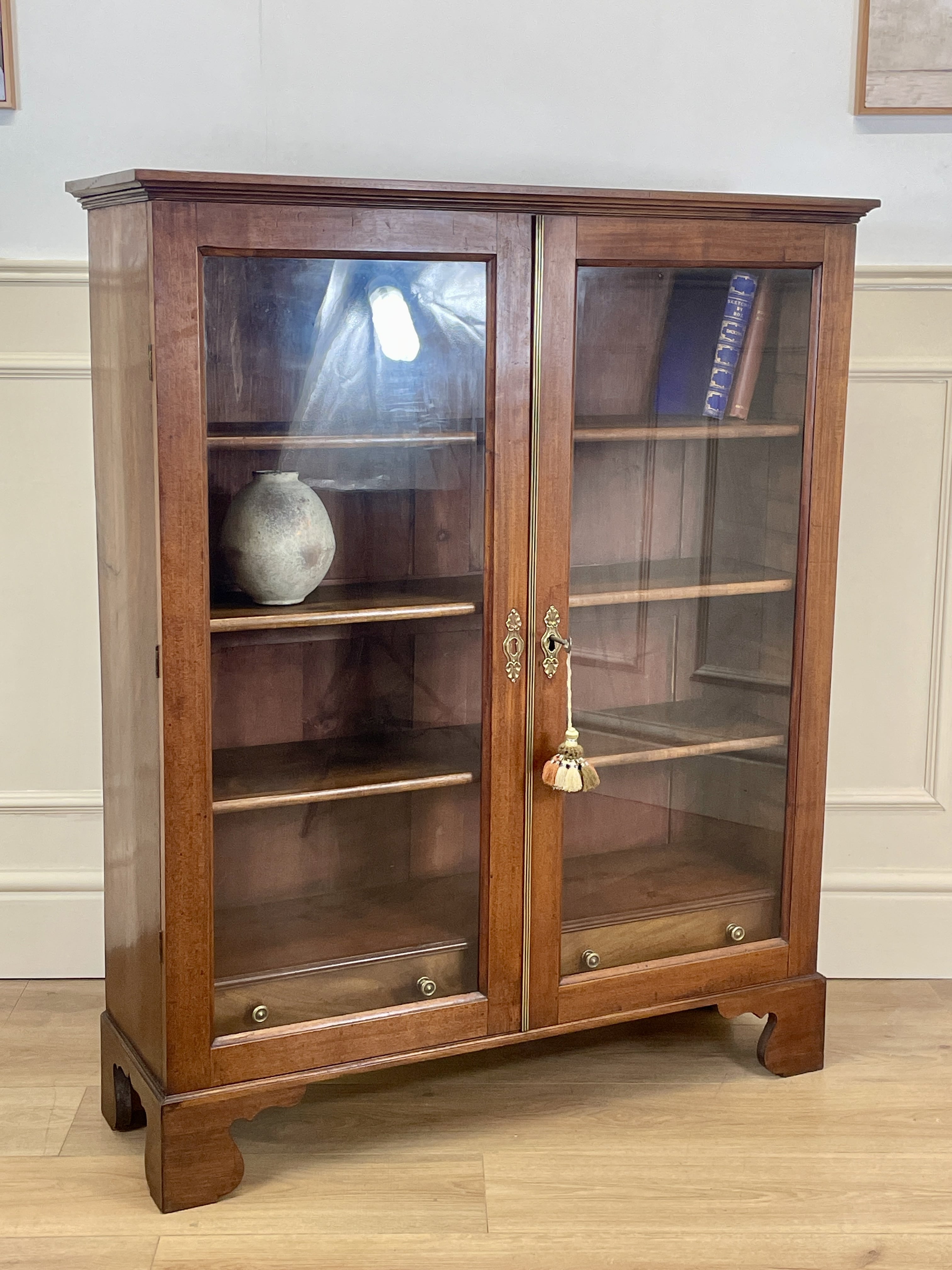 Wooden display cabinet with glass doors in a room with white paneled walls.