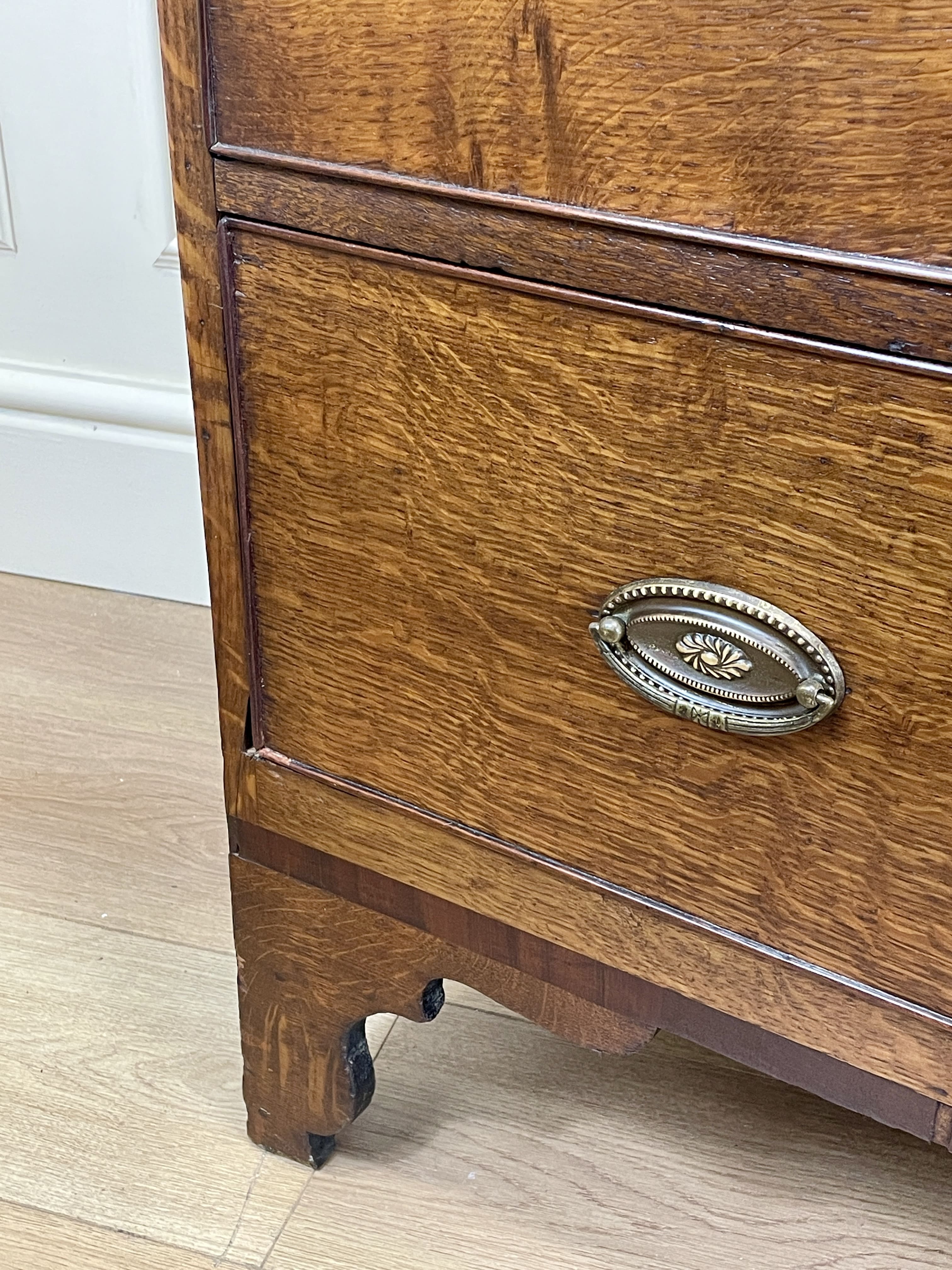 Close-up of a wooden drawer with a decorative handle on a light wood floor.