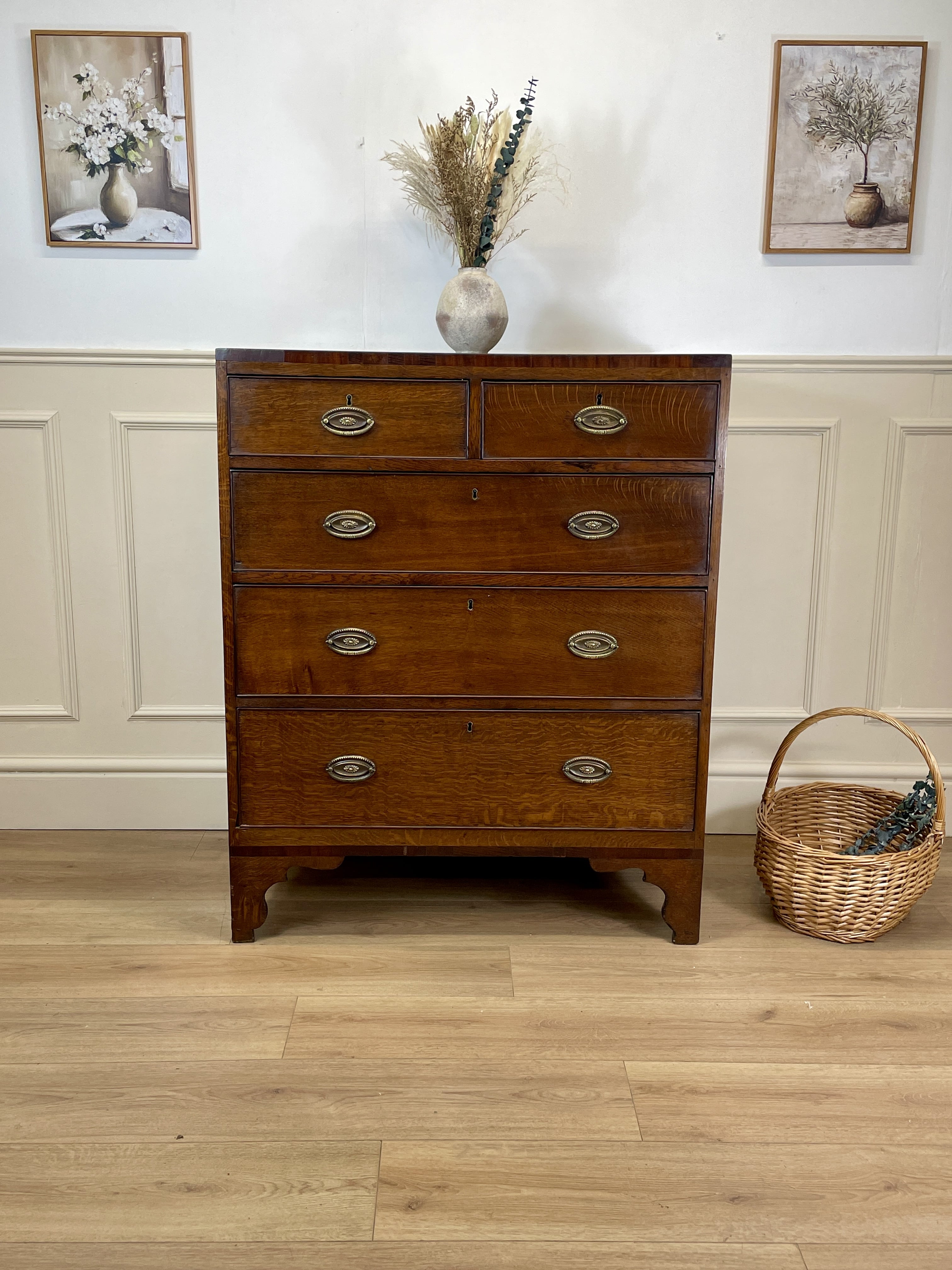 Wooden dresser with four drawers on a wooden floor, with two framed pictures on the wall.
