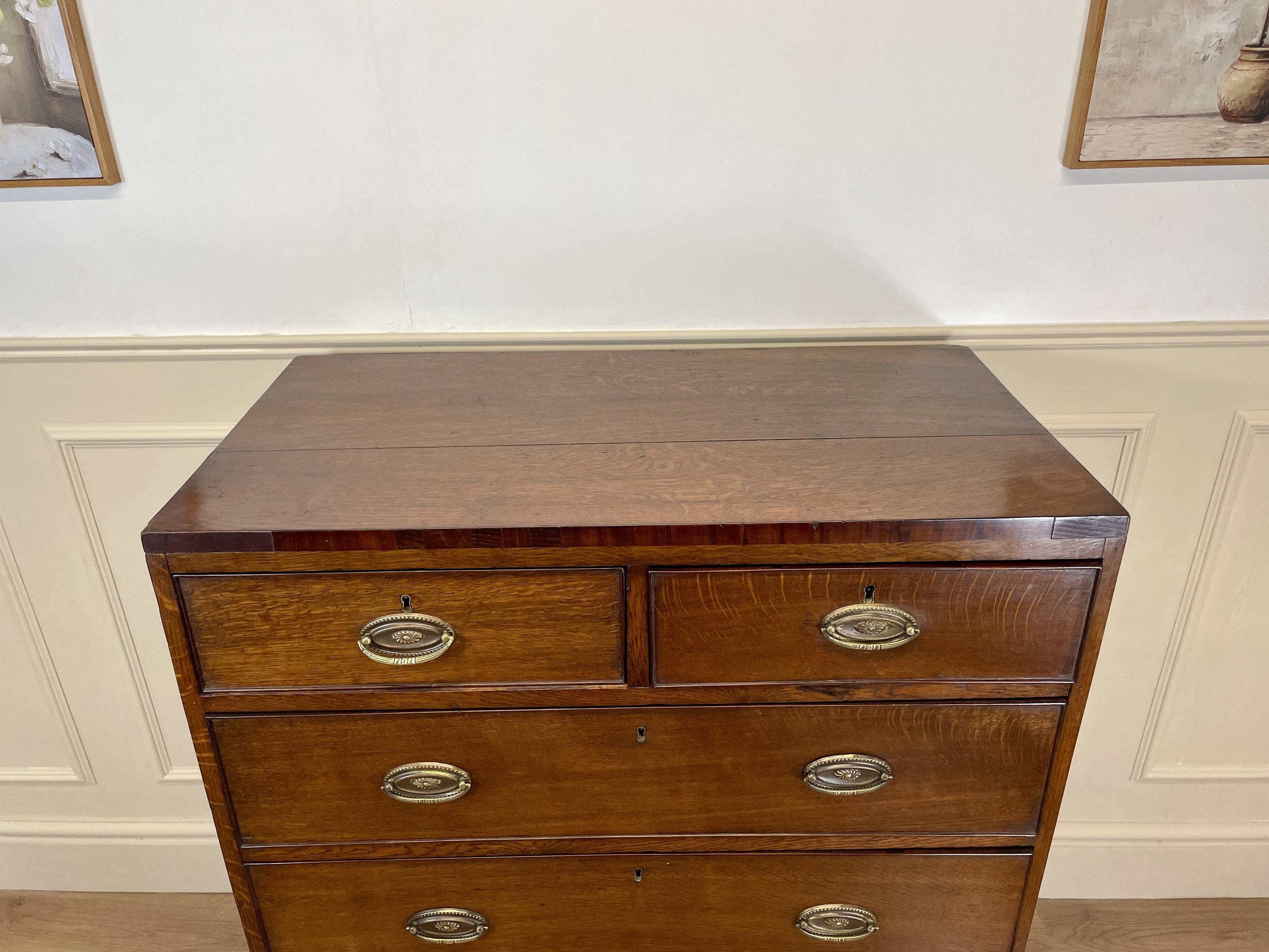 Wooden dresser with four drawers and brass handles against a white wall.