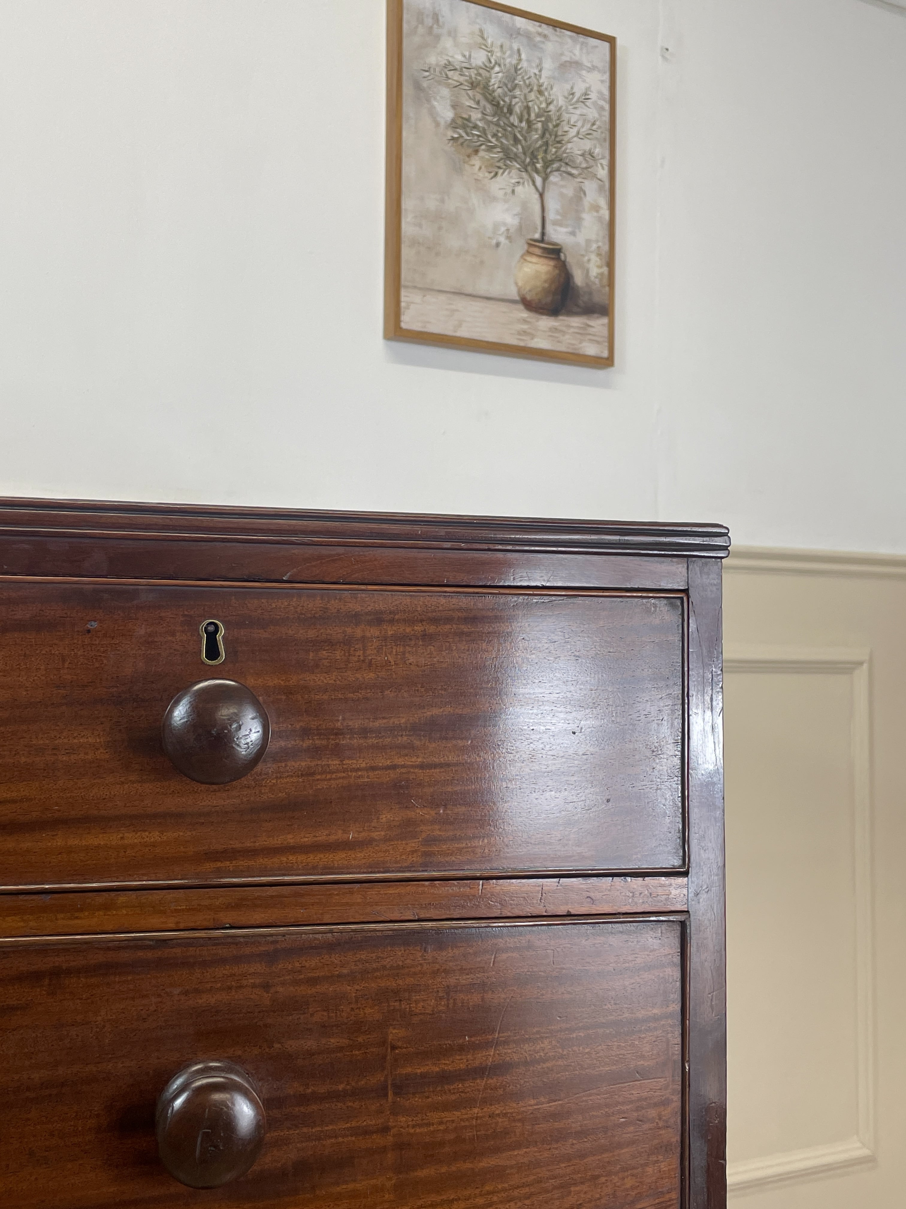 Wooden dresser with two drawers and a painting of a tree on the wall above it.