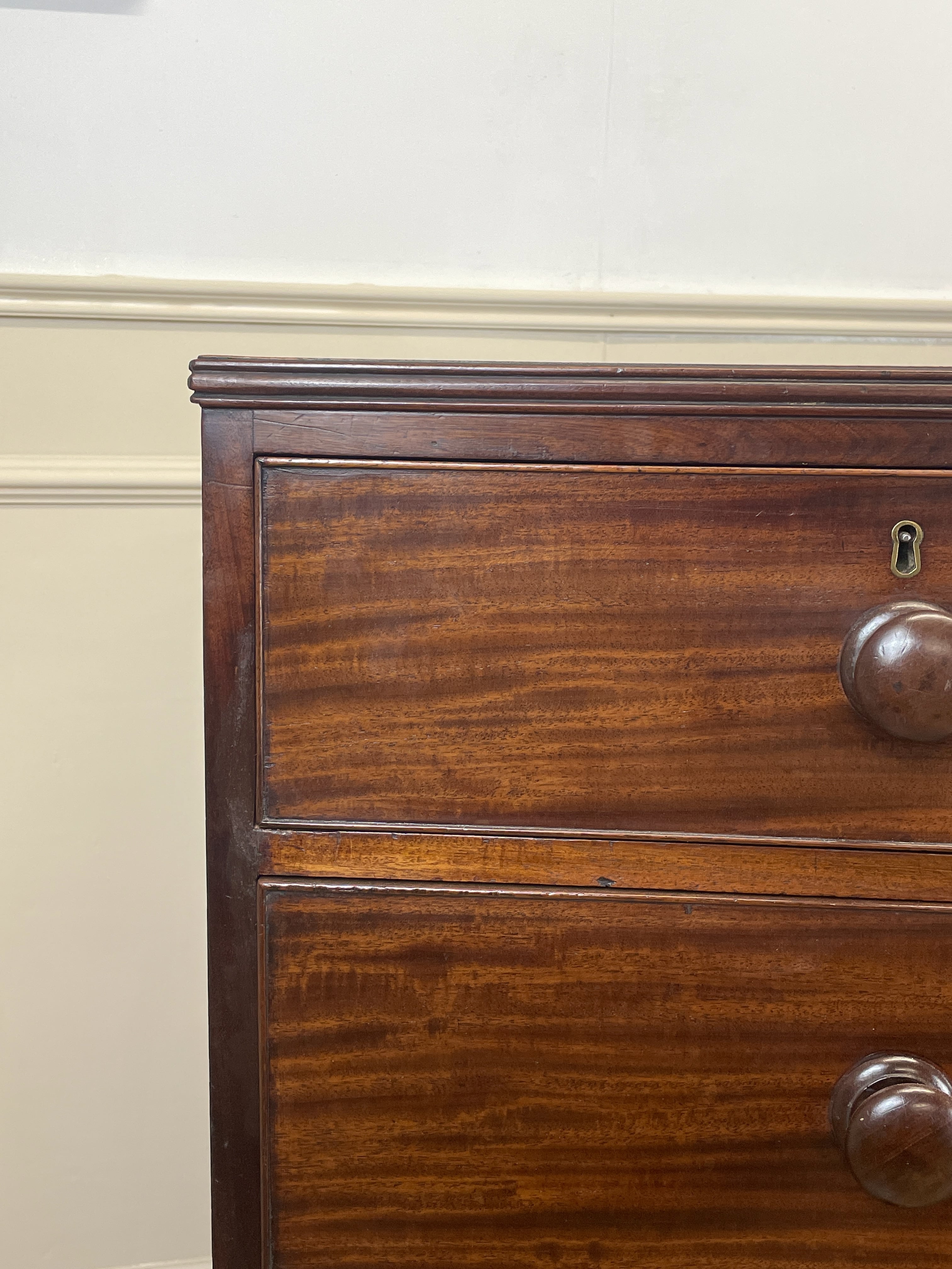Close-up of a wooden dresser with a knob on a white wall.