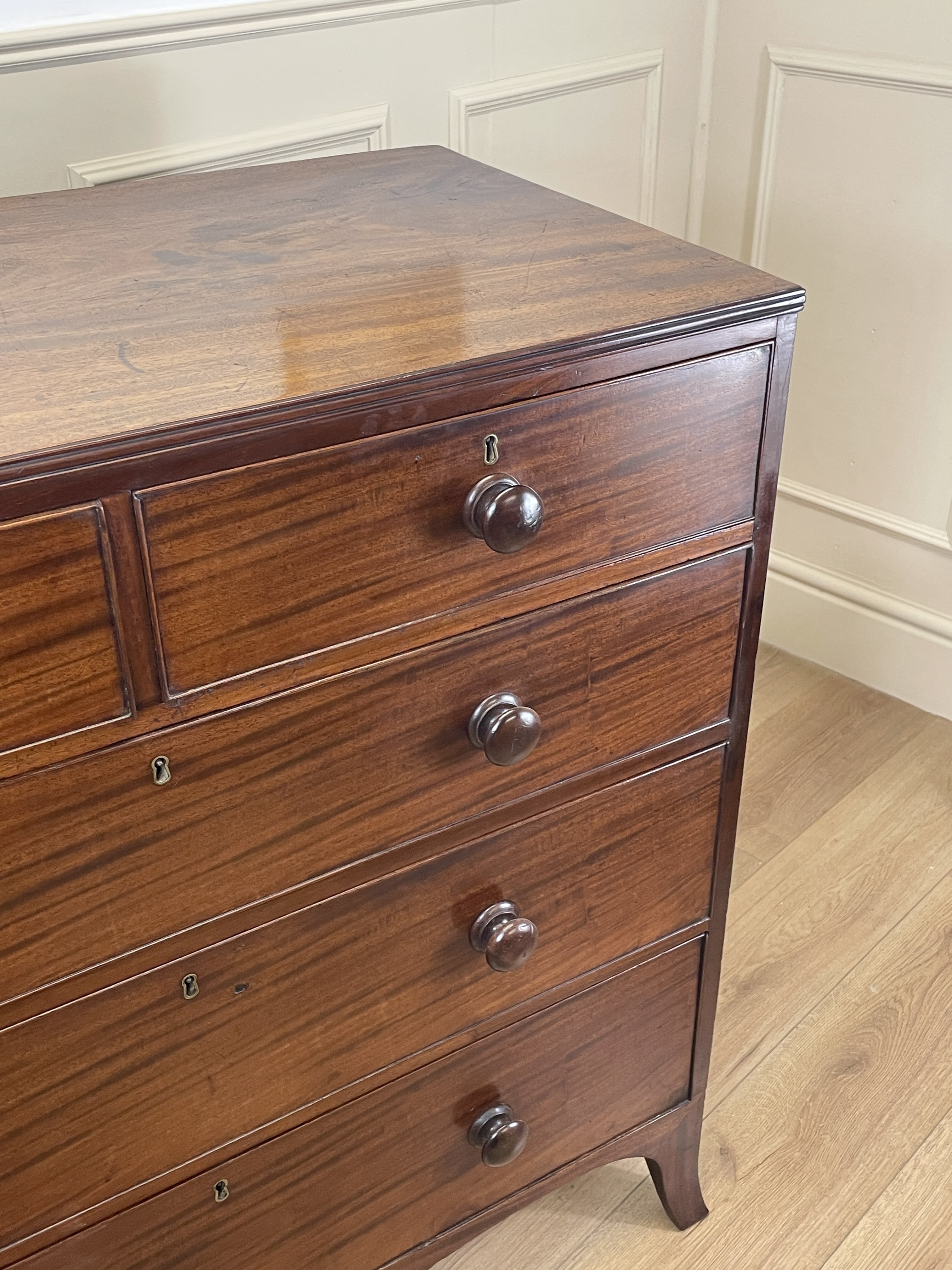 Wooden dresser with three drawers on a wooden floor against a white paneled wall.
