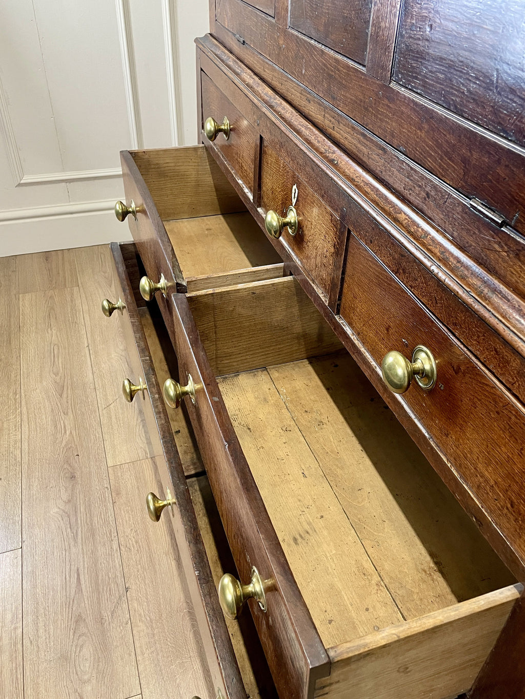 Wooden dresser with open drawers and brass handles on a wooden floor.