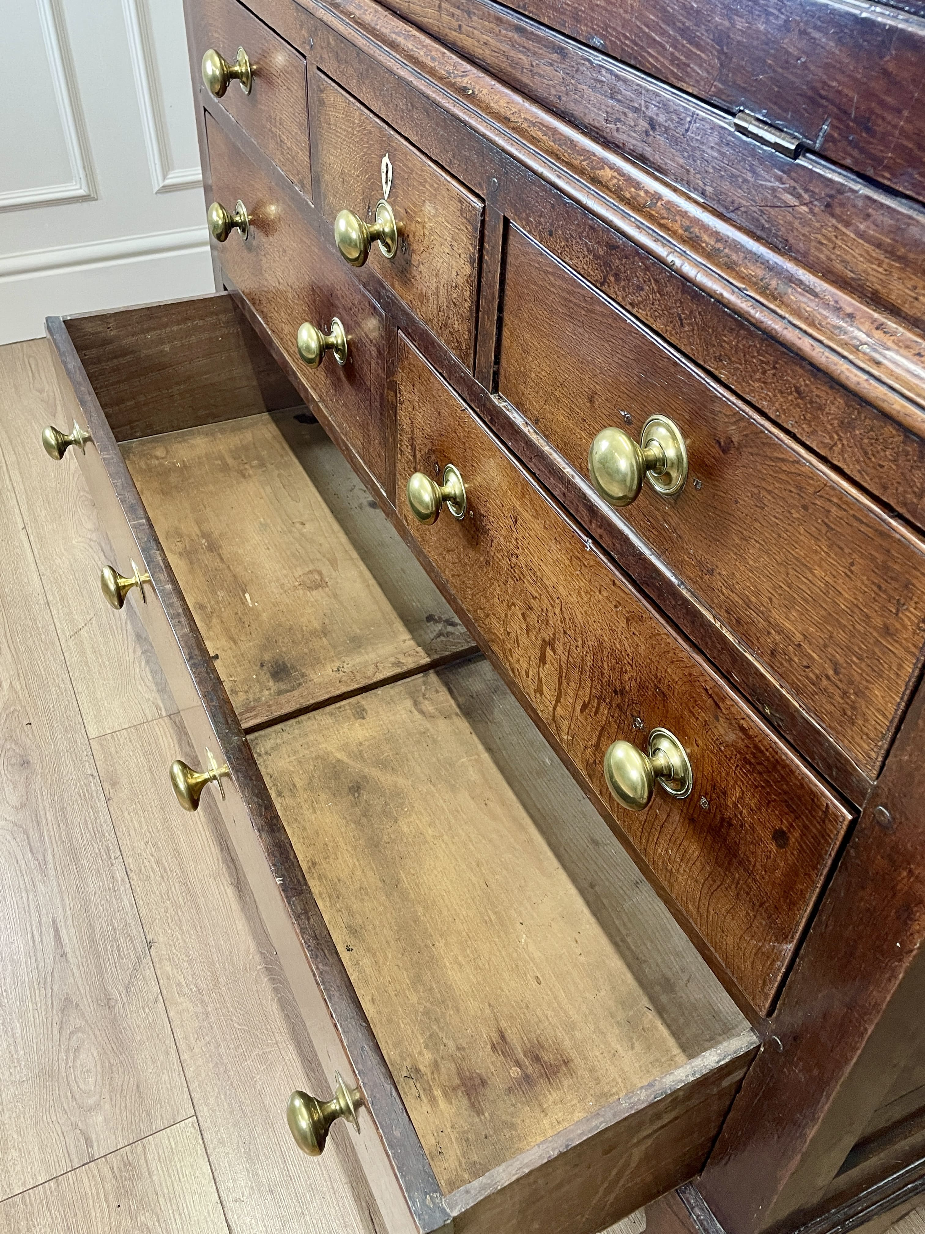Wooden dresser with open drawers and brass handles on a wooden floor.