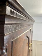 Close-up of a wooden fireplace with intricate carvings and a white wall in the background.