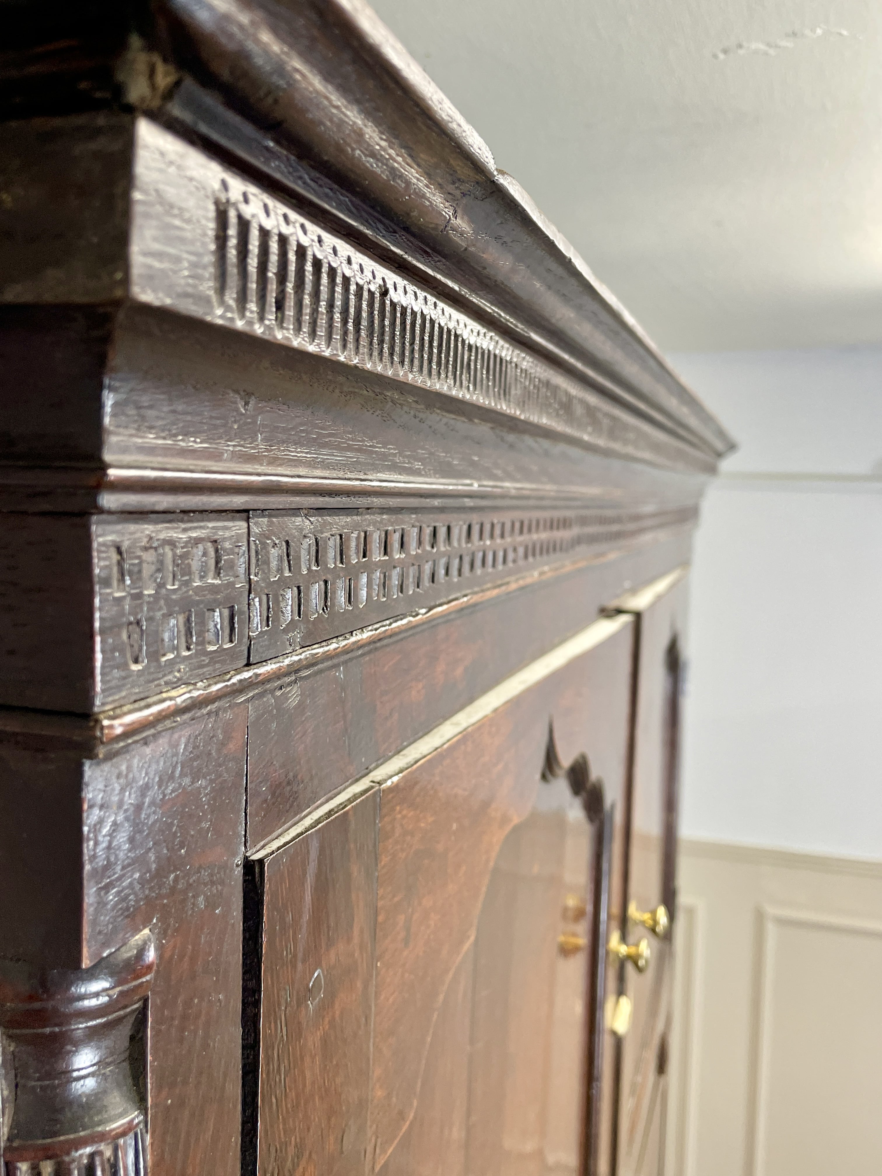 Close-up of a wooden fireplace with intricate carvings and a white wall in the background.