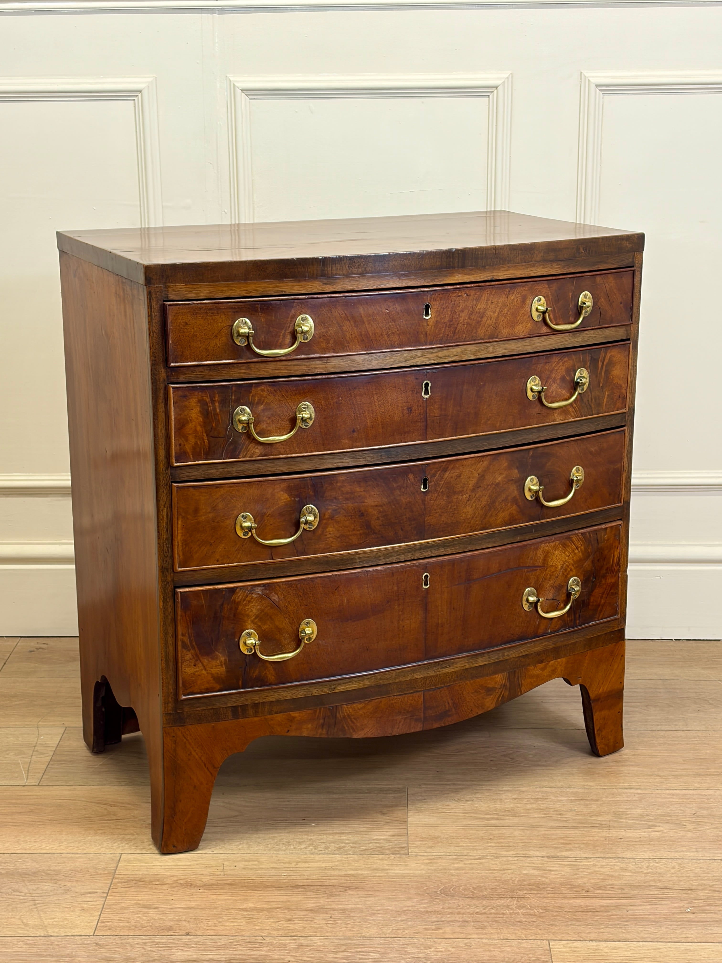 Wooden dresser with four drawers and brass handles on a wooden floor.
