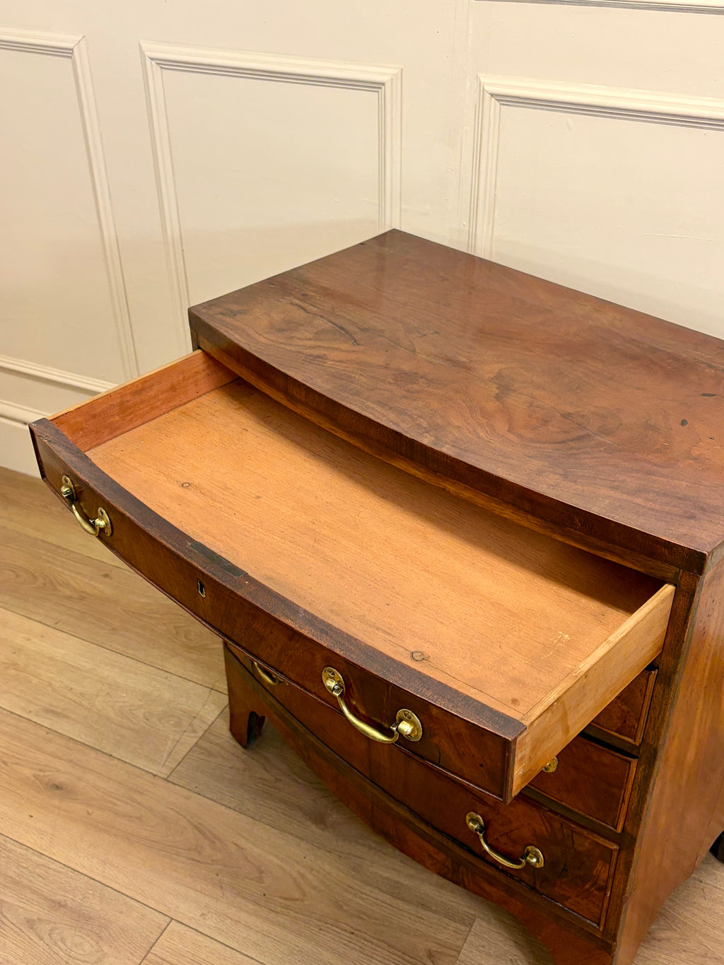Wooden dresser with open drawer against a white paneled wall.