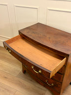 Wooden dresser with open drawer against a white paneled wall.