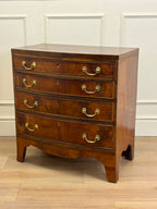 Wooden dresser with four drawers and brass handles on a wooden floor.