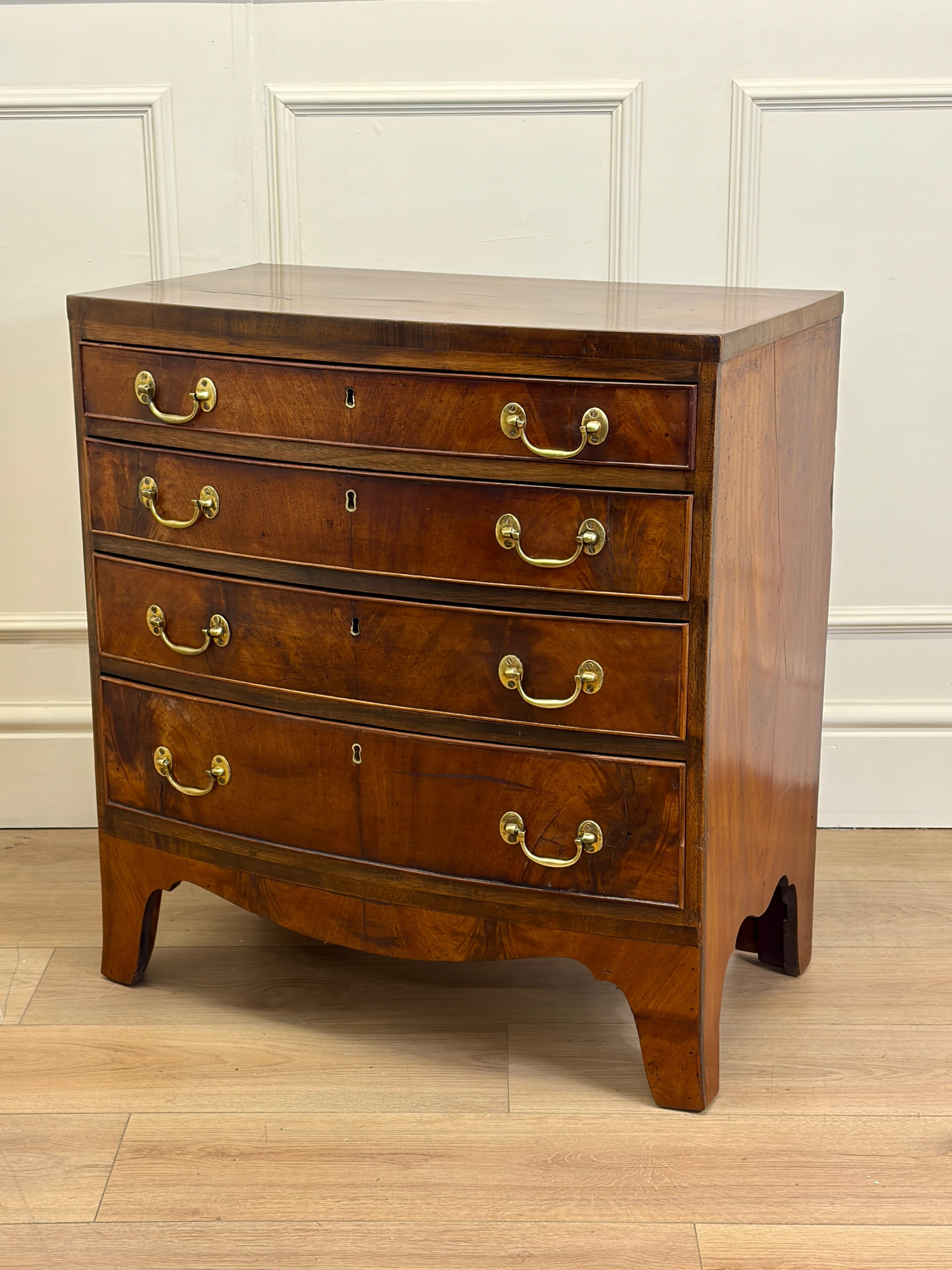 Wooden dresser with four drawers and brass handles on a wooden floor.
