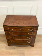 Wooden dresser with curved design and brass handles against a white paneled wall.