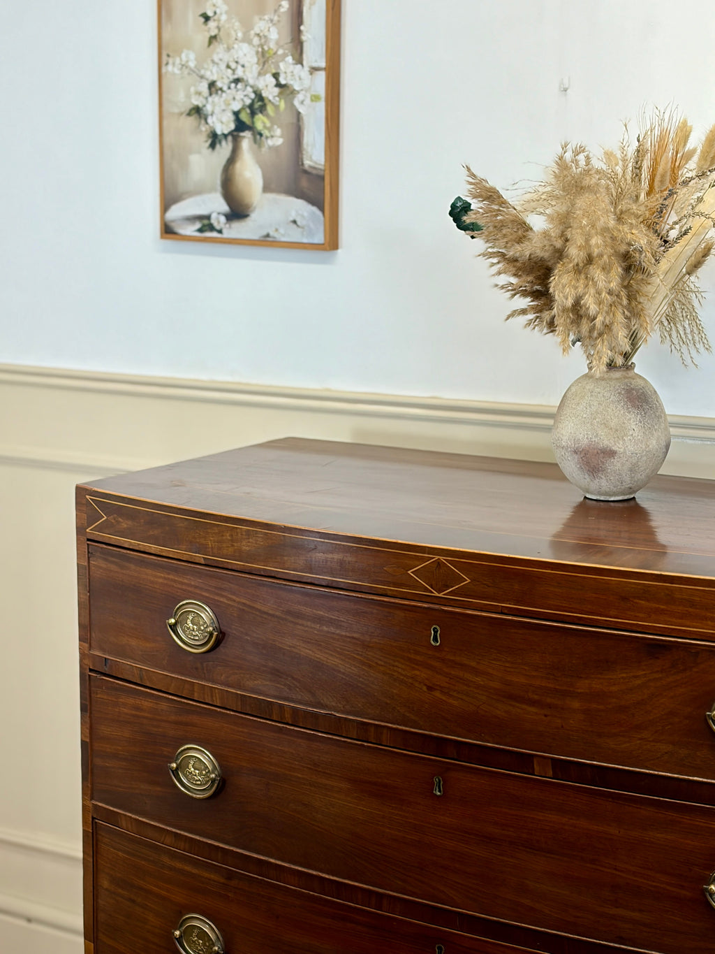 Wooden dresser with decorative vase and dried plants against a light wall.