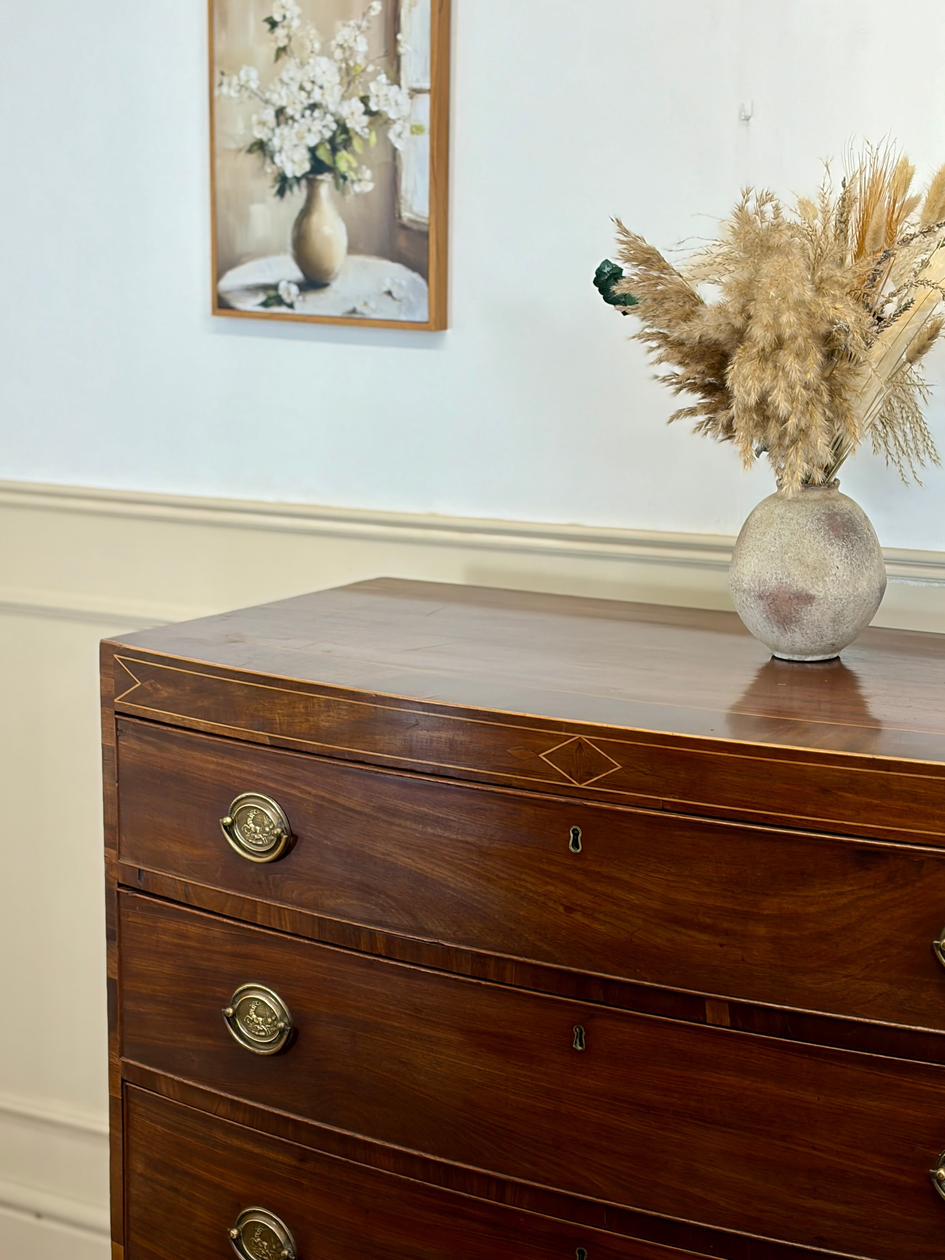 Wooden dresser with decorative vase and dried plants against a light wall.