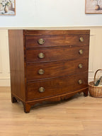 Wooden dresser with brass handles in a room with a light blue wall and wooden floor.