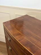 Wooden dresser with a curved top against a white paneled wall.