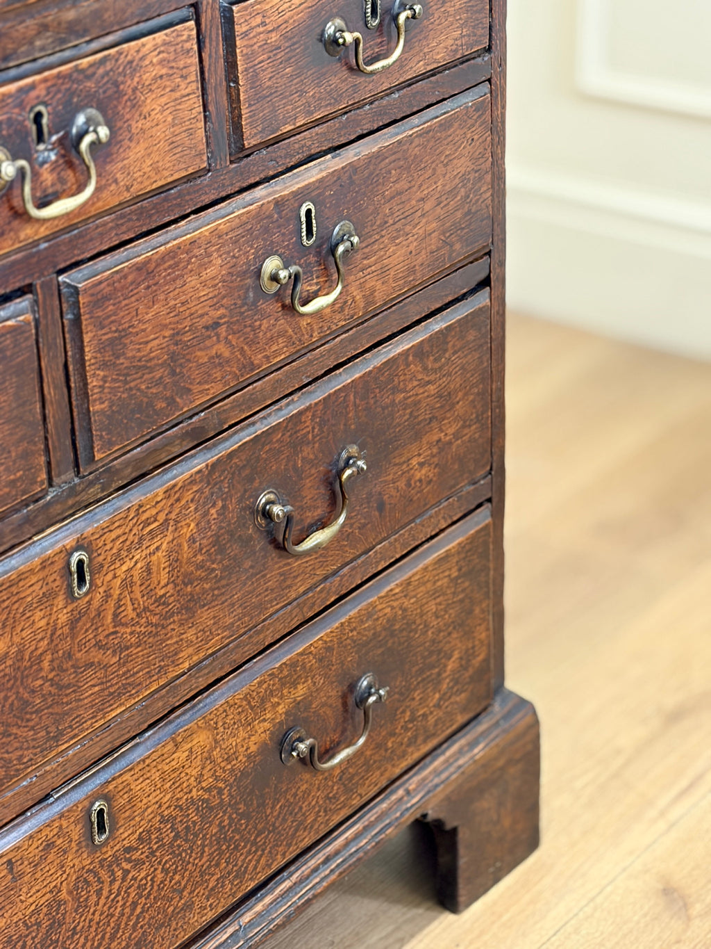 Close-up of a wooden dresser with drawers and brass handles on a light wood floor.