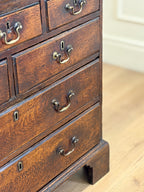 Close-up of a wooden dresser with drawers and brass handles on a light wood floor.