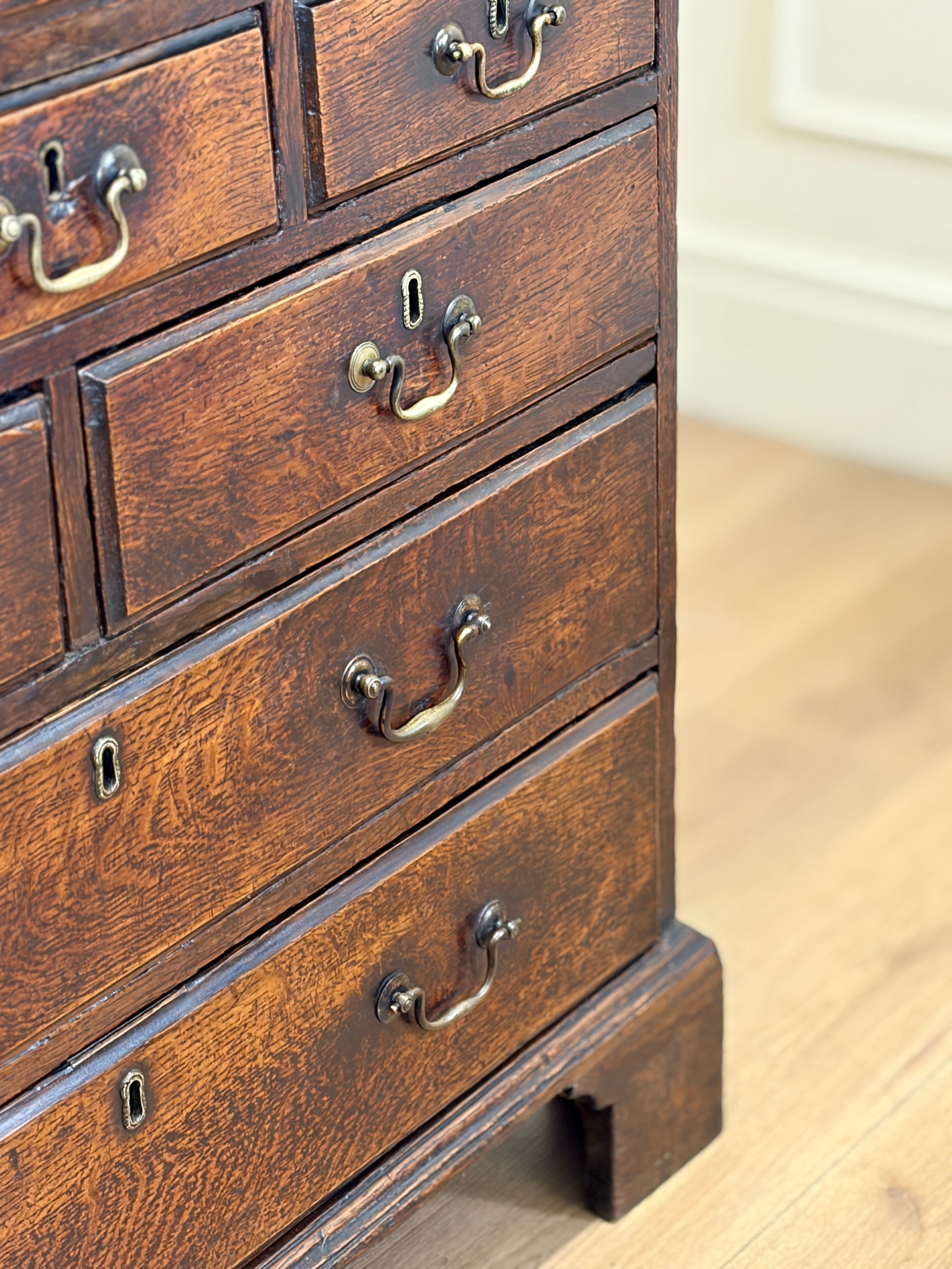 Close-up of a wooden dresser with drawers and brass handles on a light wood floor.