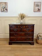 Wooden dresser with decorative items in a room with wainscoting and framed pictures.