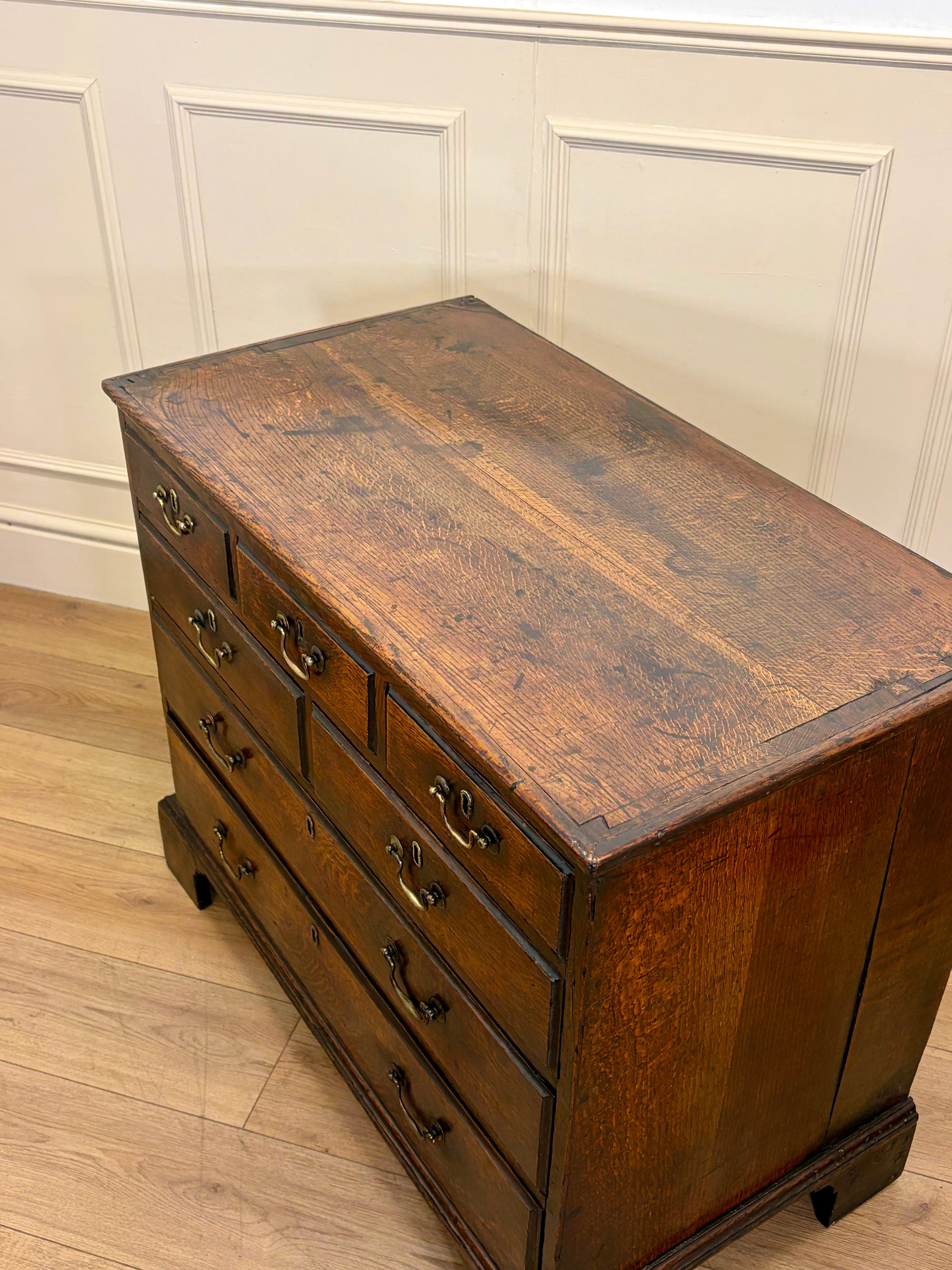 Wooden chest with drawers against a white paneled wall.