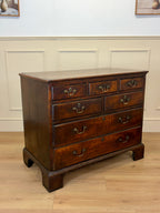 Wooden dresser with multiple drawers on a wooden floor against a white paneled wall.