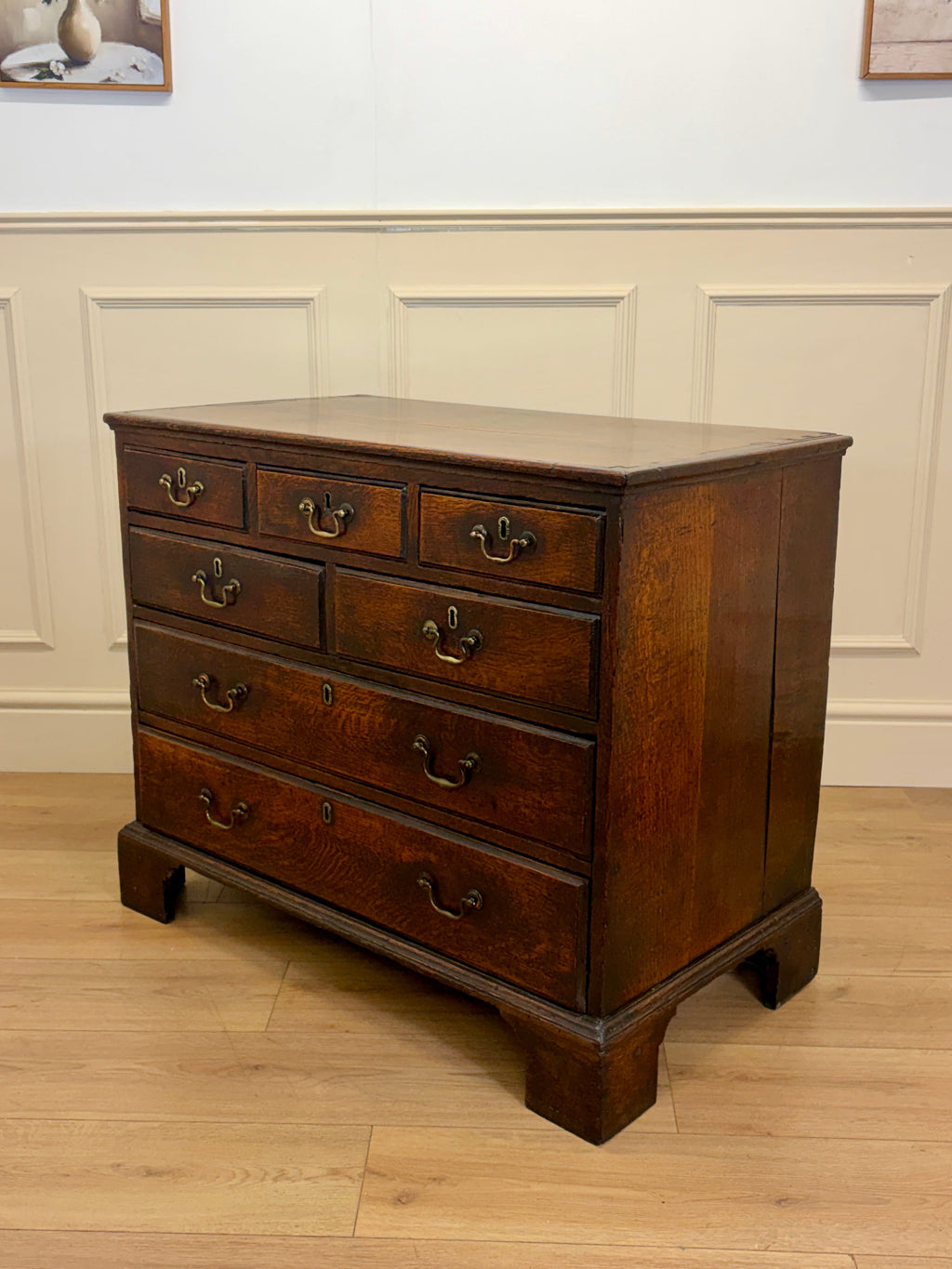 Wooden dresser with multiple drawers on a wooden floor against a white paneled wall.