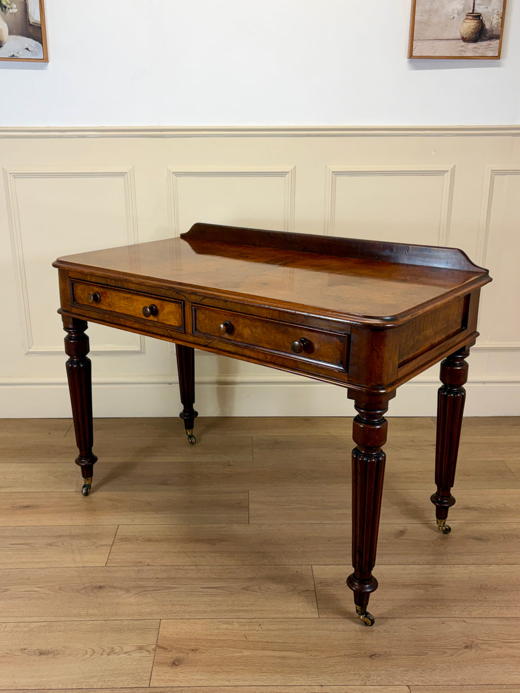 Wooden desk with drawers on a wooden floor against a white paneled wall.