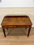 Wooden desk with a classical design on a wooden floor against a white paneled wall.