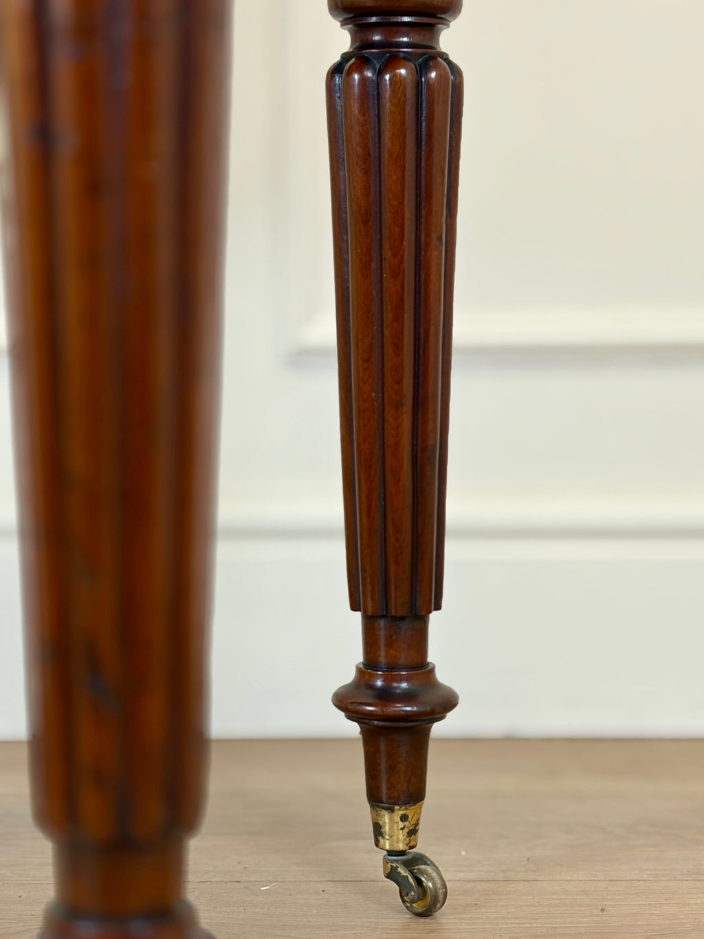 Close-up of a wooden leg with a wheel on a light wood floor.