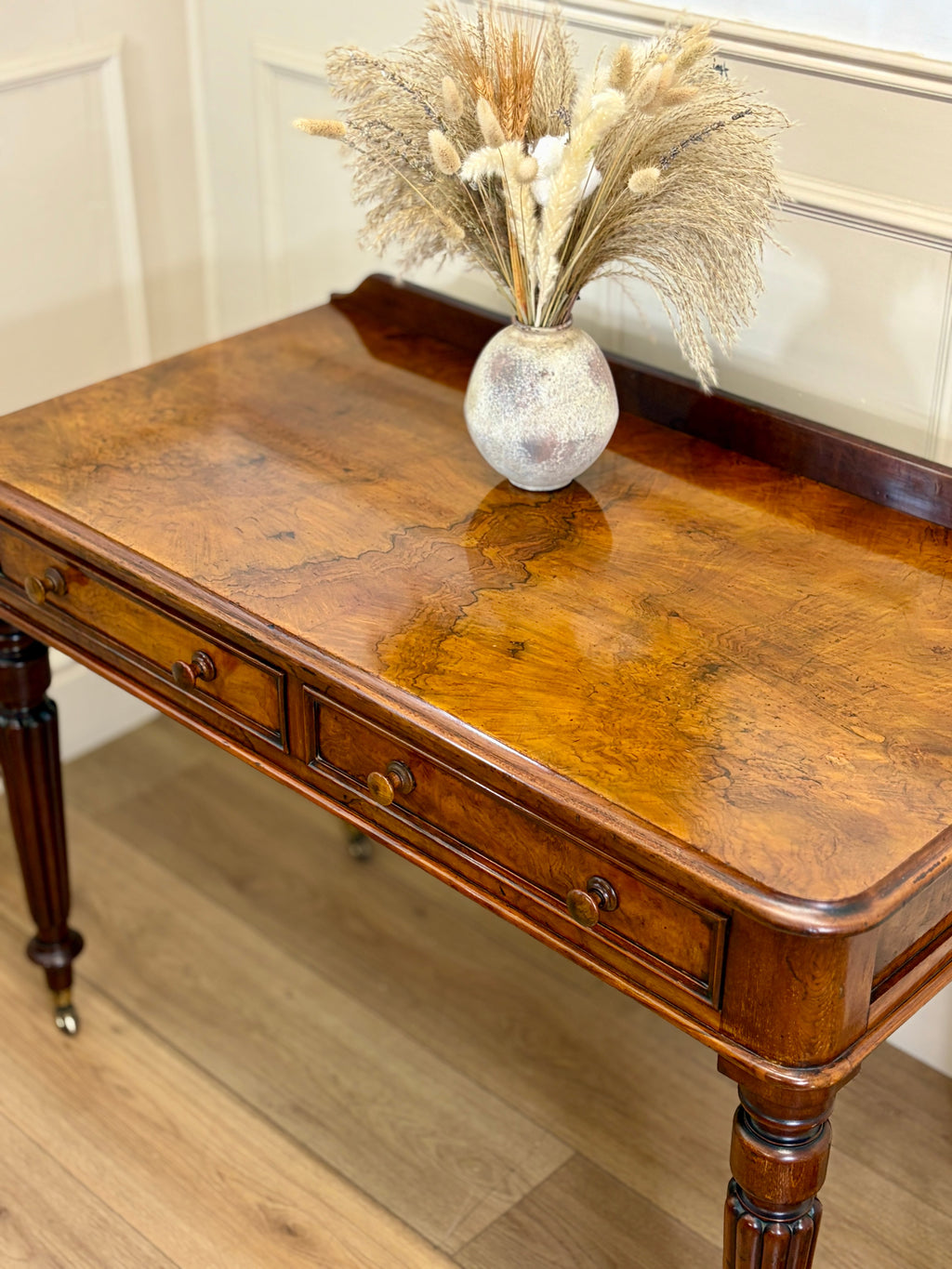 Wooden desk with a vase of dried flowers on a wooden floor.