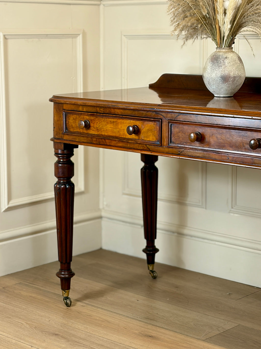 Wooden console table with a vase of dried plants against a paneled wall.