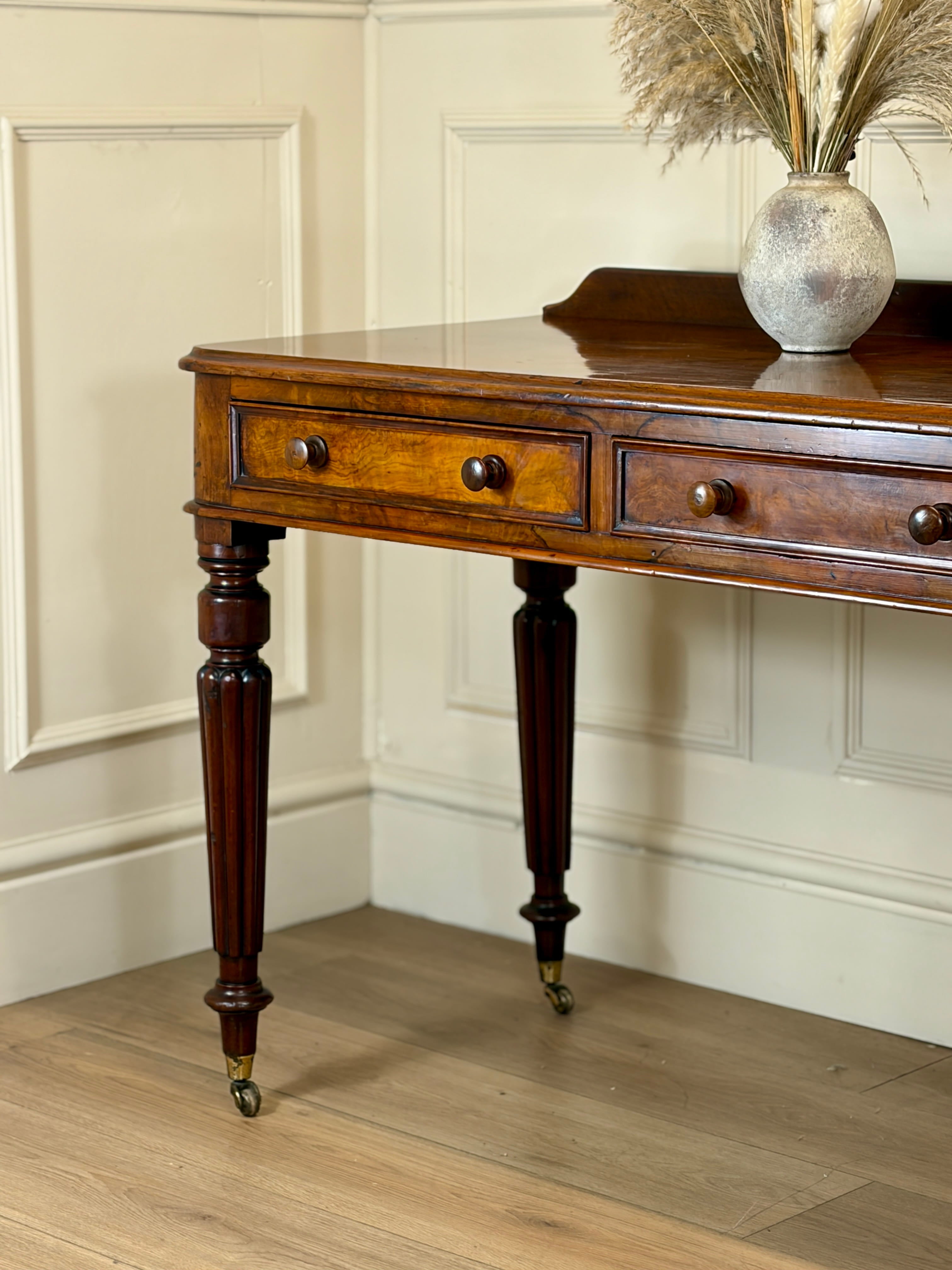 Wooden console table with a vase of dried plants against a paneled wall.