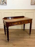 Wooden desk with drawers on a wooden floor against a white paneled wall.