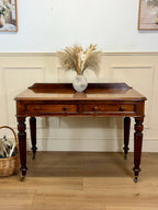 Wooden desk with decorative items in a room with light-colored walls and wooden floor.