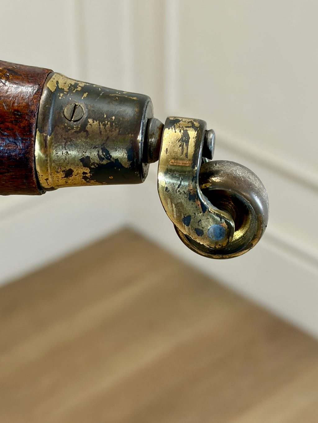 Close-up of a brass hook attached to a wooden handle with a white wall background