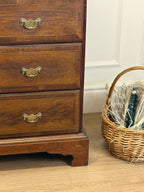 Wooden dresser with brass handles next to a wicker basket on a wooden floor.