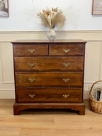 Wooden dresser with four drawers on a wooden floor, with a vase of dried plants on top.